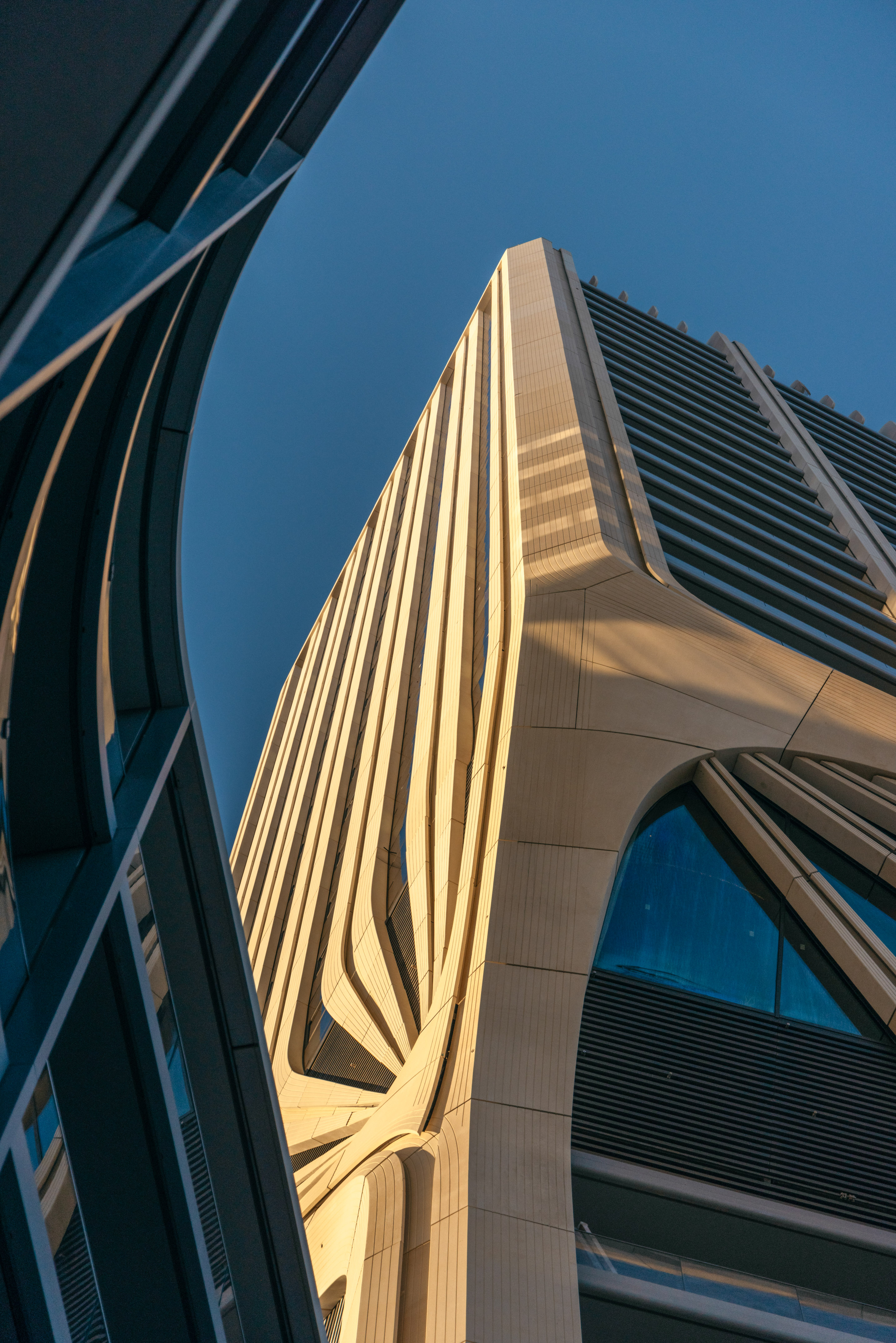 Modern skyscraper with undulating beige facade under clear blue sky.
