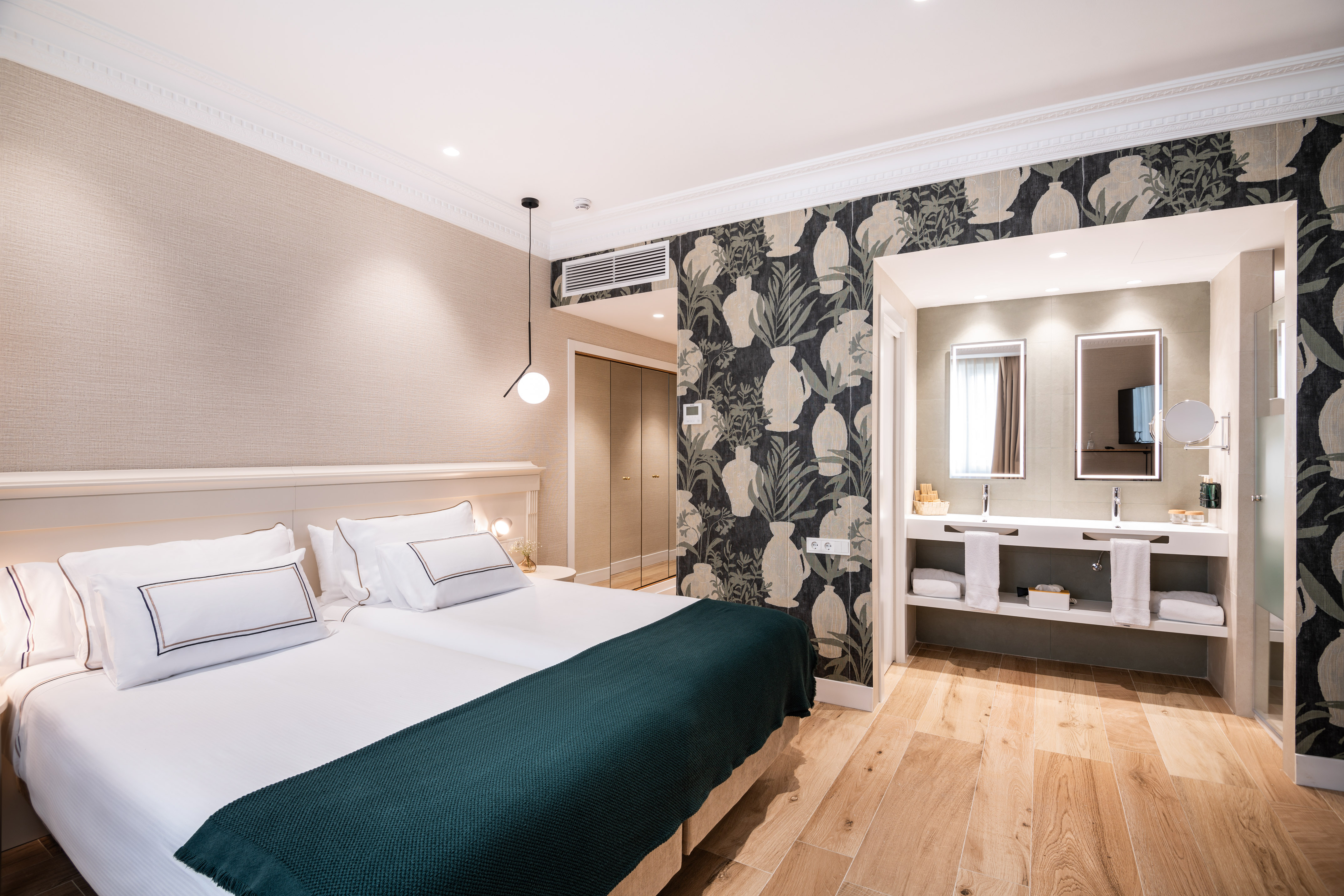 Modern hotel room with twin beds, green throw, and open bathroom with double vanity.