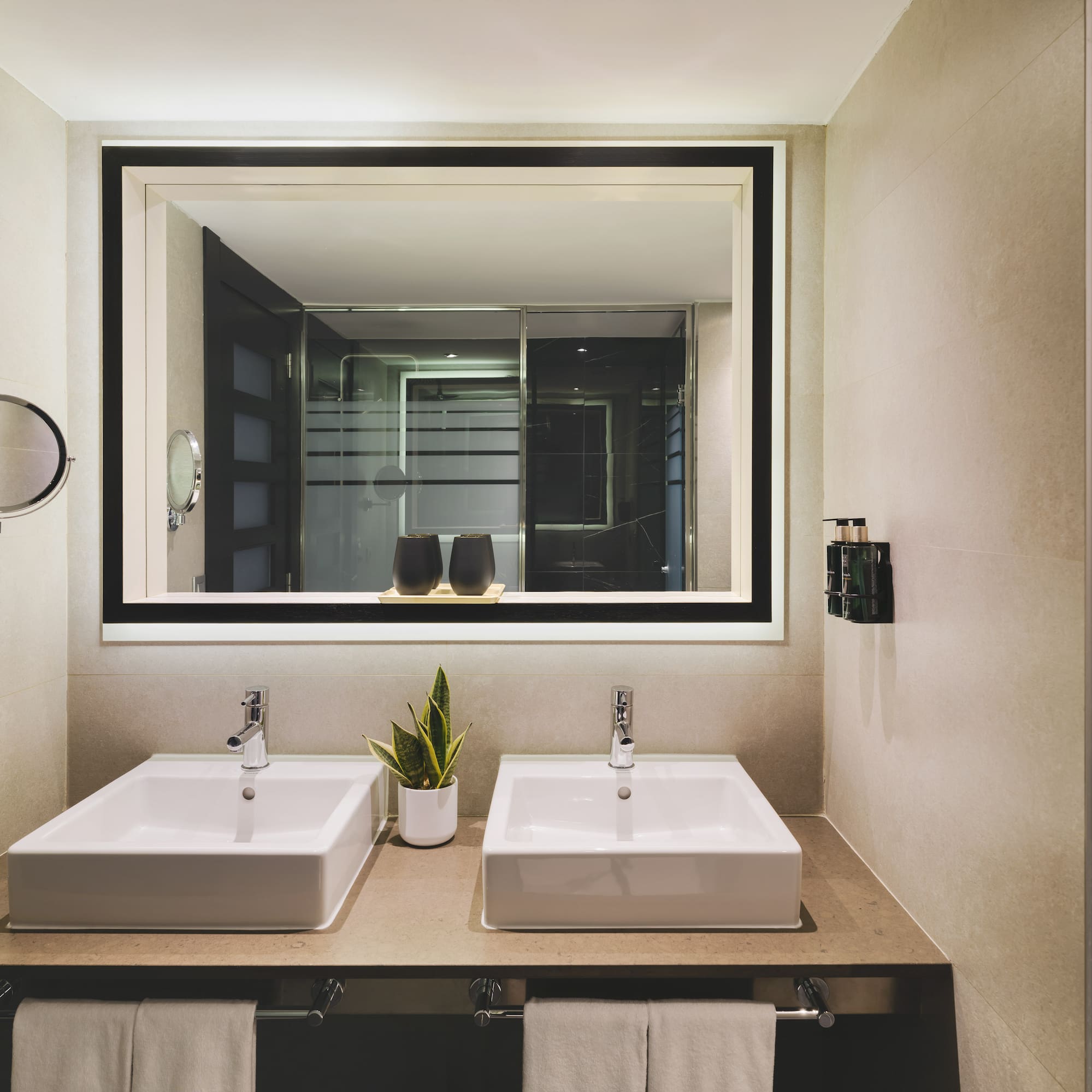 Baño de hotel moderno con doble lavabo y espejo iluminado.