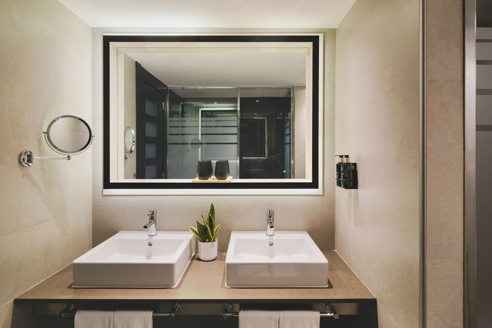 Baño de hotel moderno con doble lavabo y espejo iluminado.