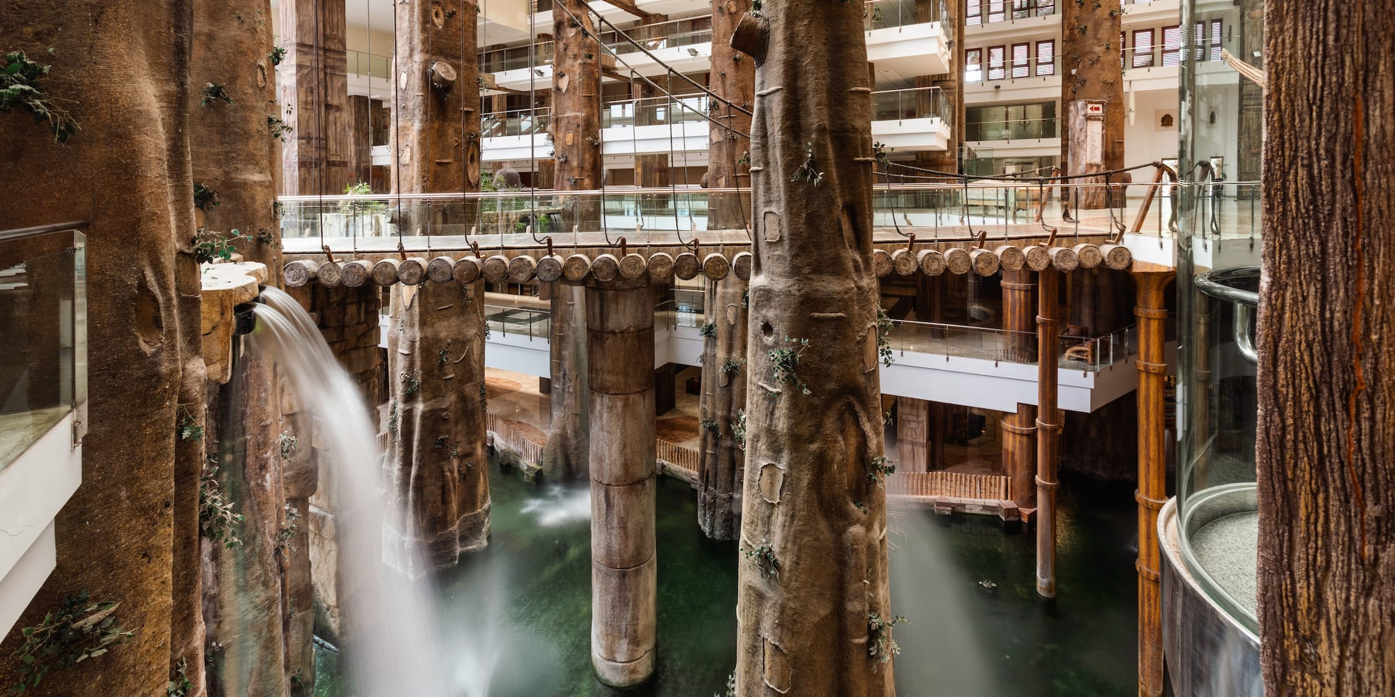 Indoor hotel atrium with tree-like columns, waterfalls, and bridges.