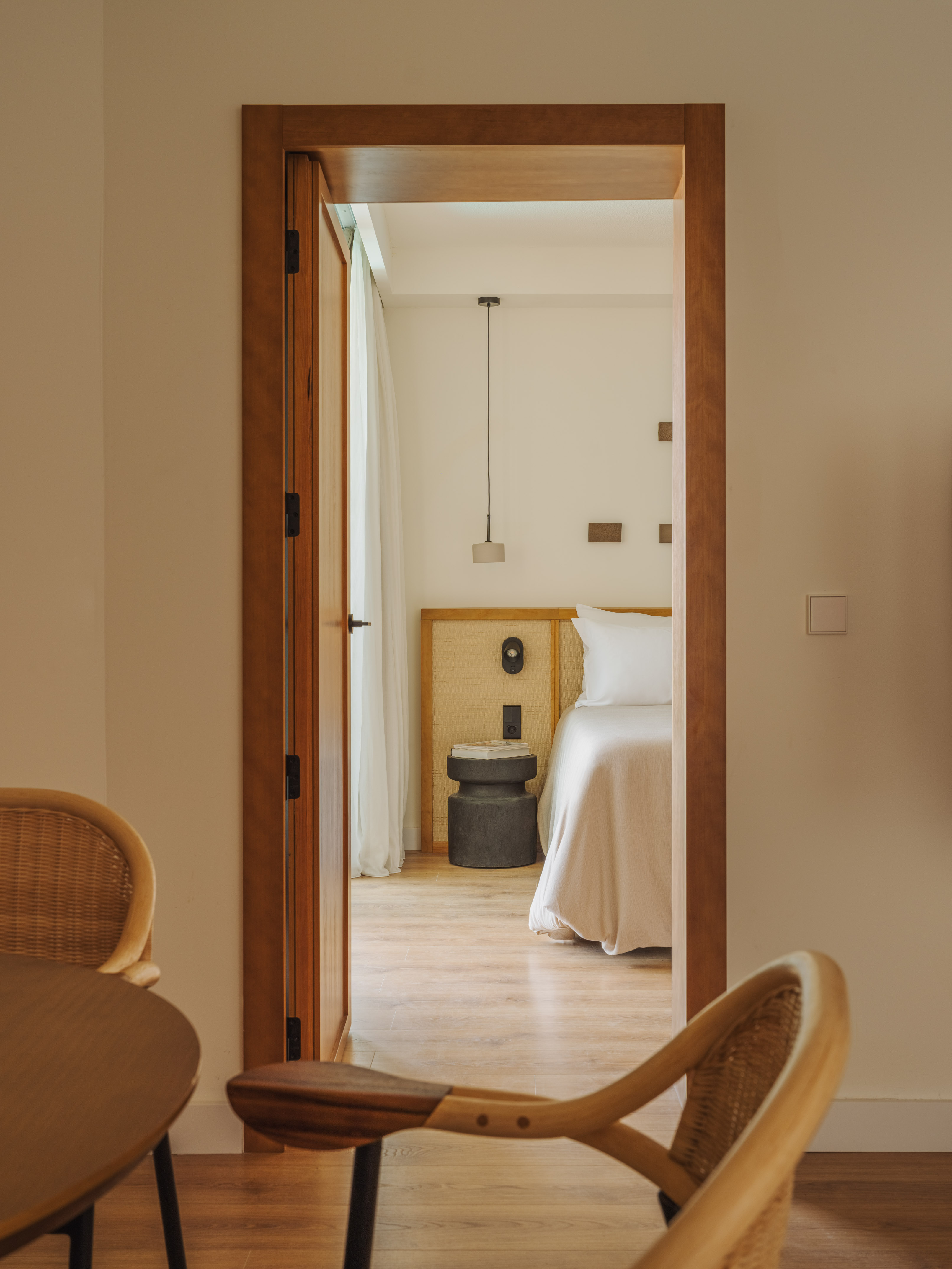 Bedroom with white bed and nightstand, seen through open wooden door.