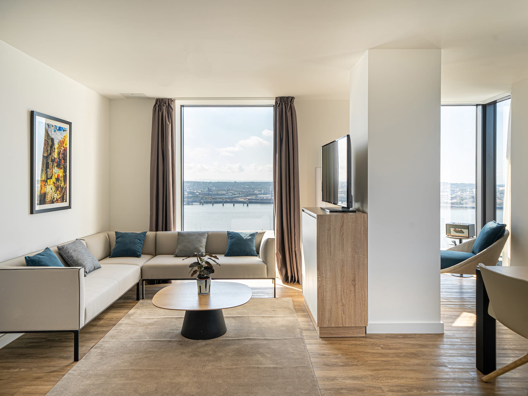 Contemporary living room with L-shaped sofa, water city view, and wood floors.