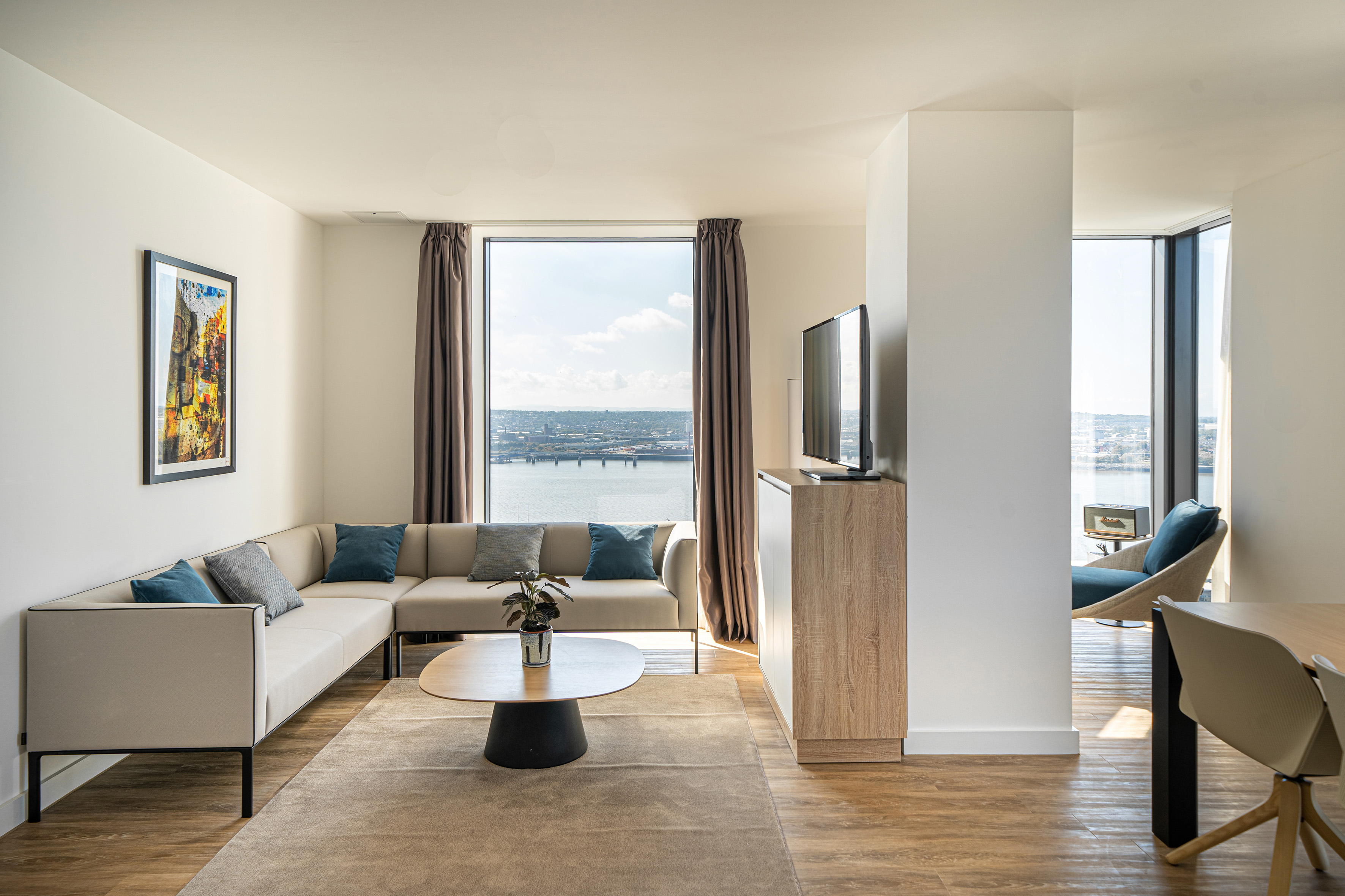 Contemporary living room with L-shaped sofa, water city view, and wood floors.