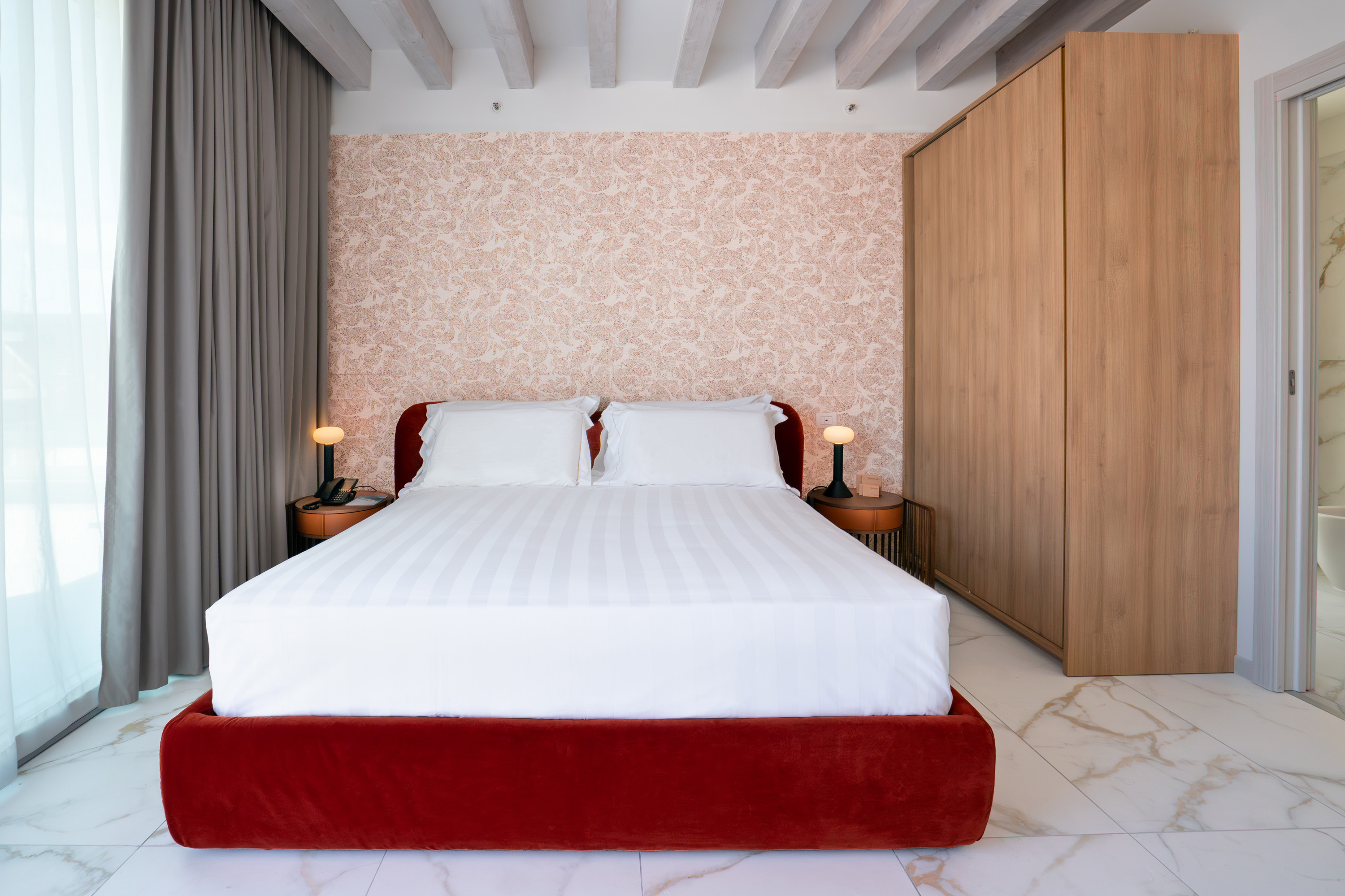 Modern bedroom with red velvet bed, patterned wallpaper, wood wardrobe, marble.