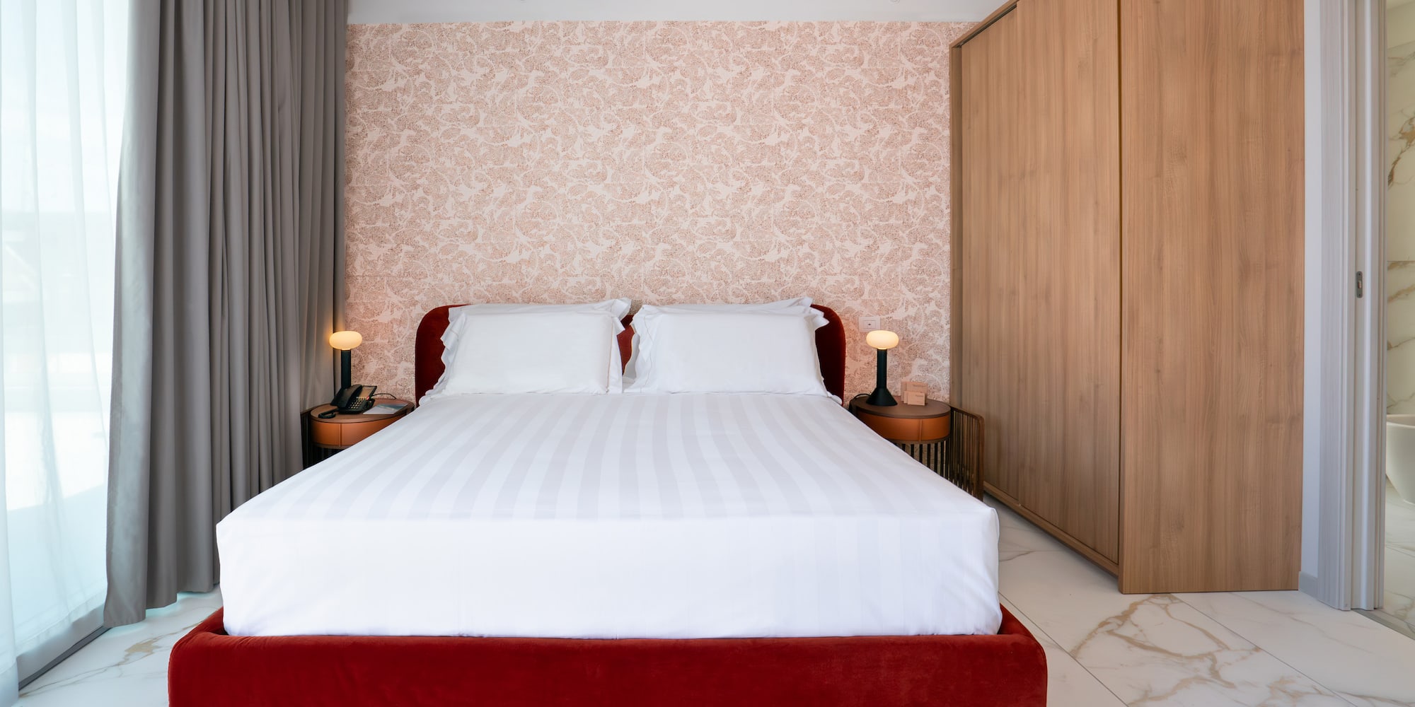 Modern bedroom with red velvet bed, patterned wallpaper, wood wardrobe, marble.