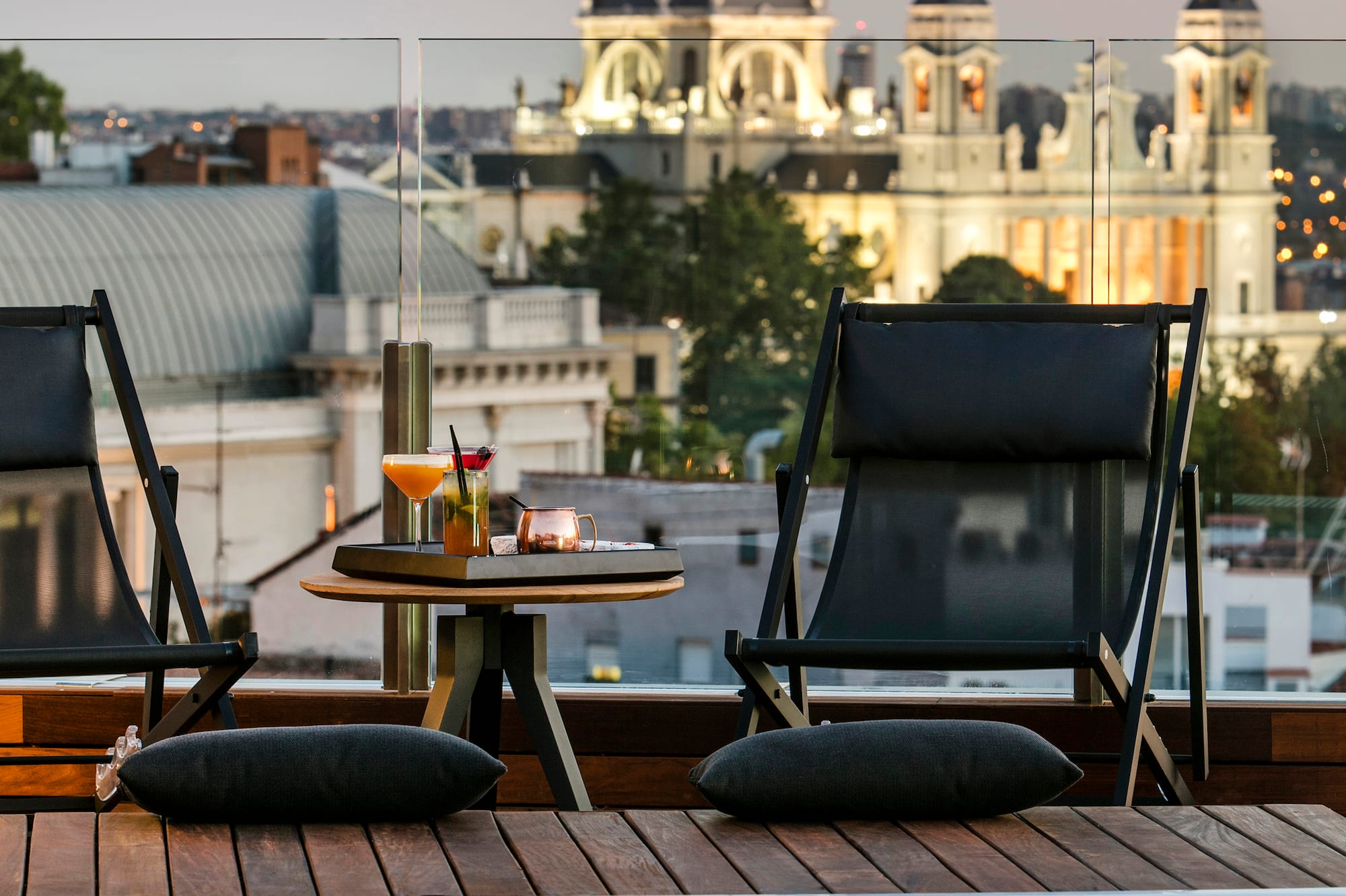 a pool with a table and chairs on a rooftop with a city in the background