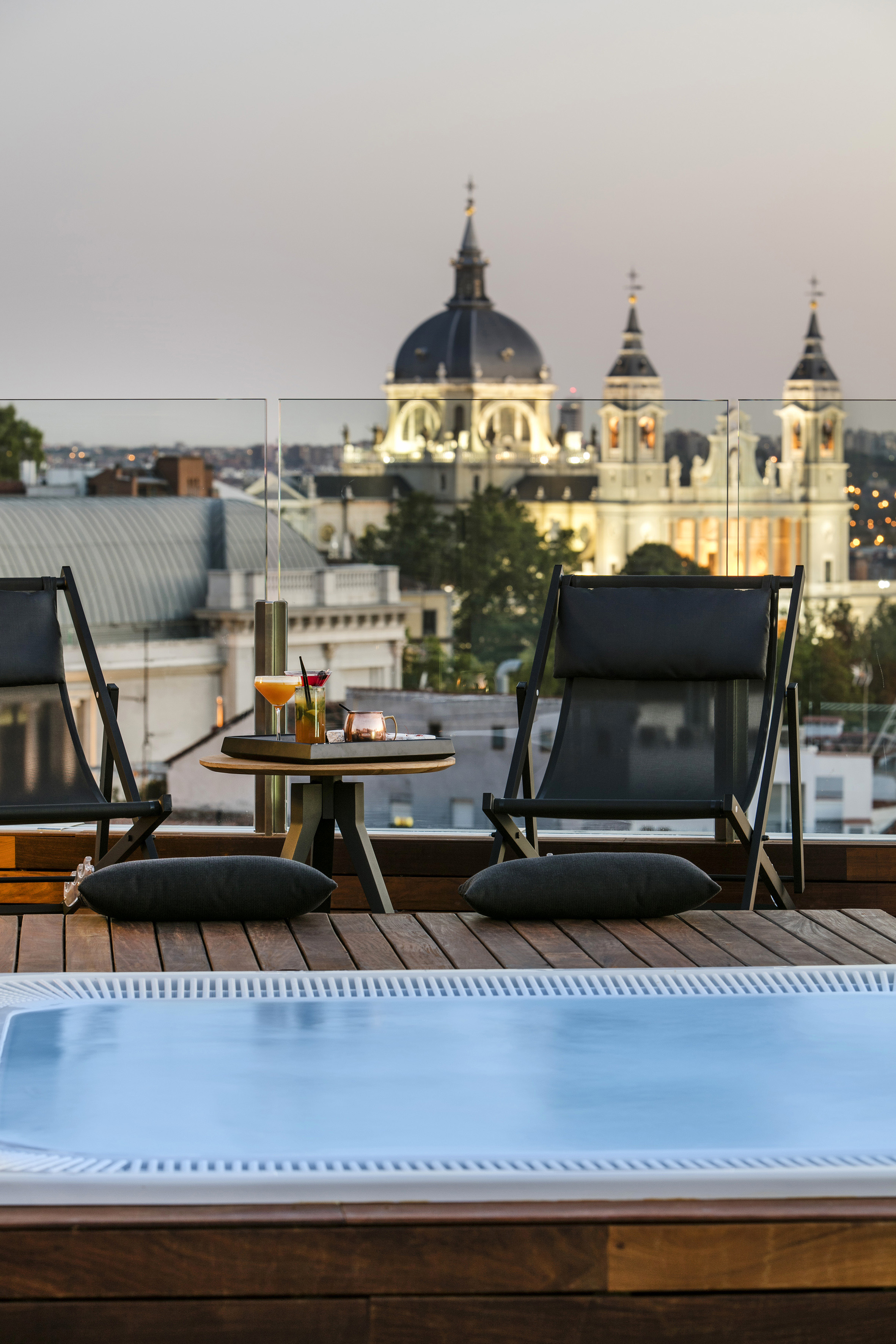 a pool with a table and chairs on a rooftop with a city in the background