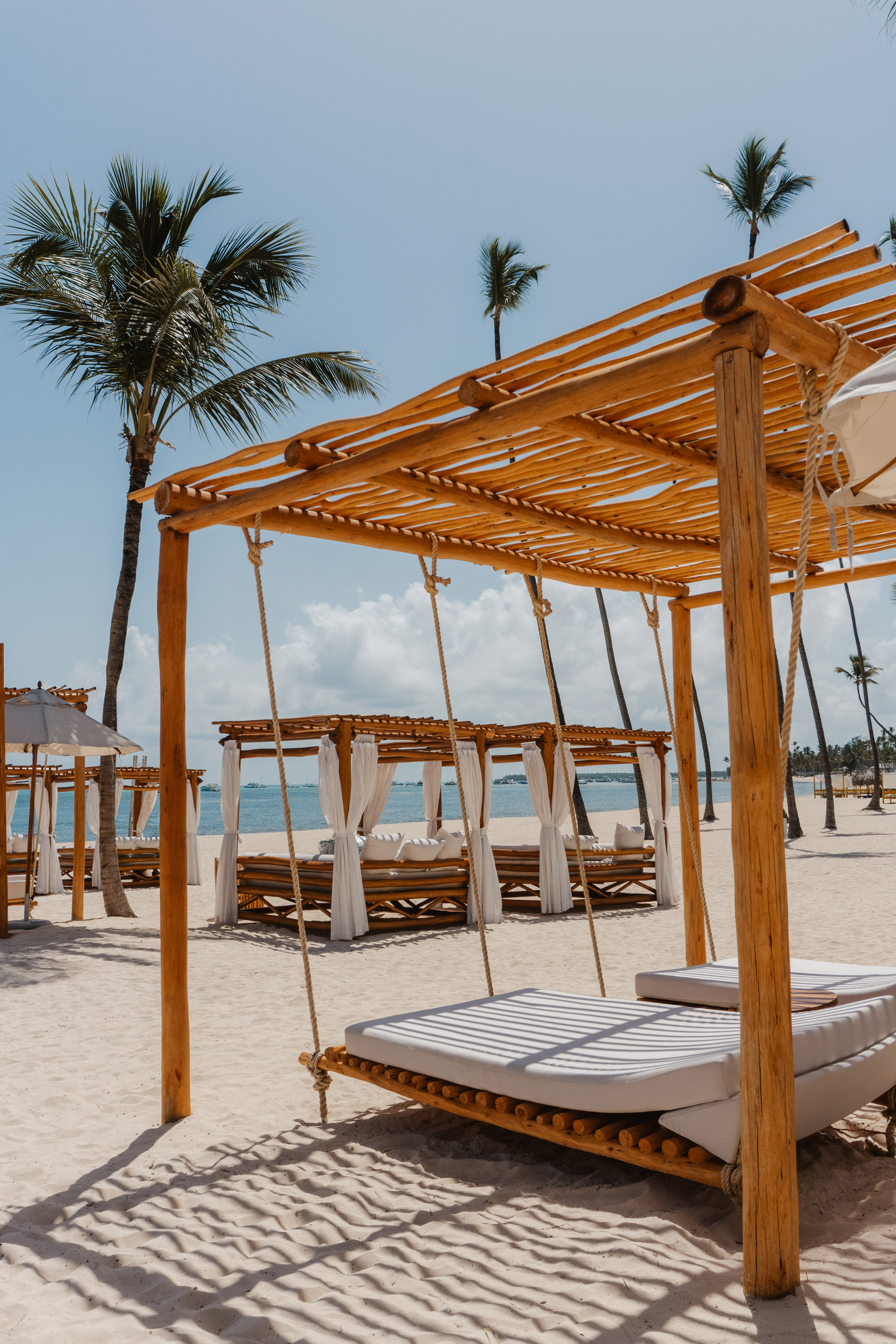 Beach cabanas with swing beds, palm trees, and ocean view.