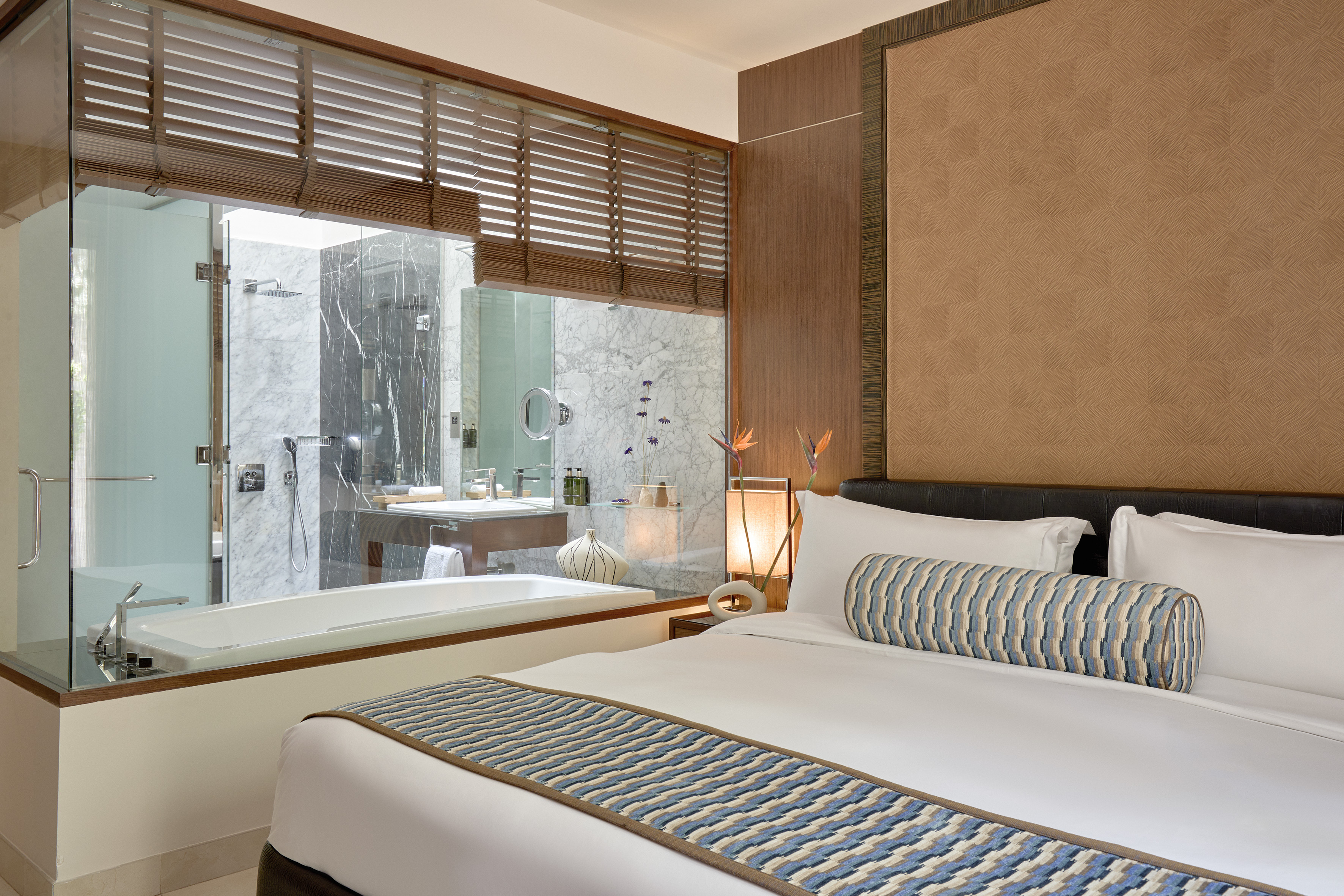 Modern hotel bedroom suite with glass-walled bathroom and bathtub.