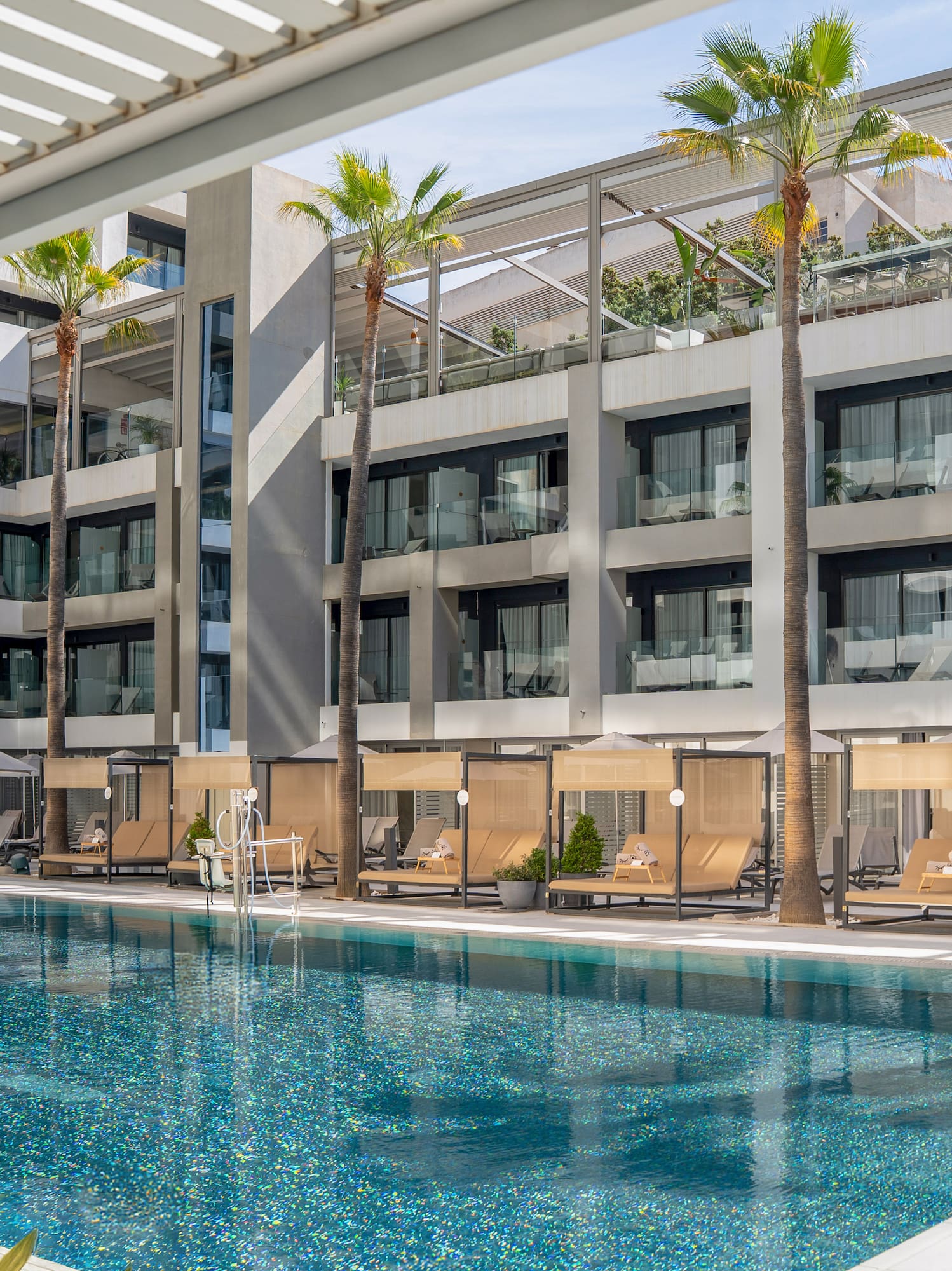 Sparkling blue hotel pool with modern architecture, palm trees, and poolside daybeds.
