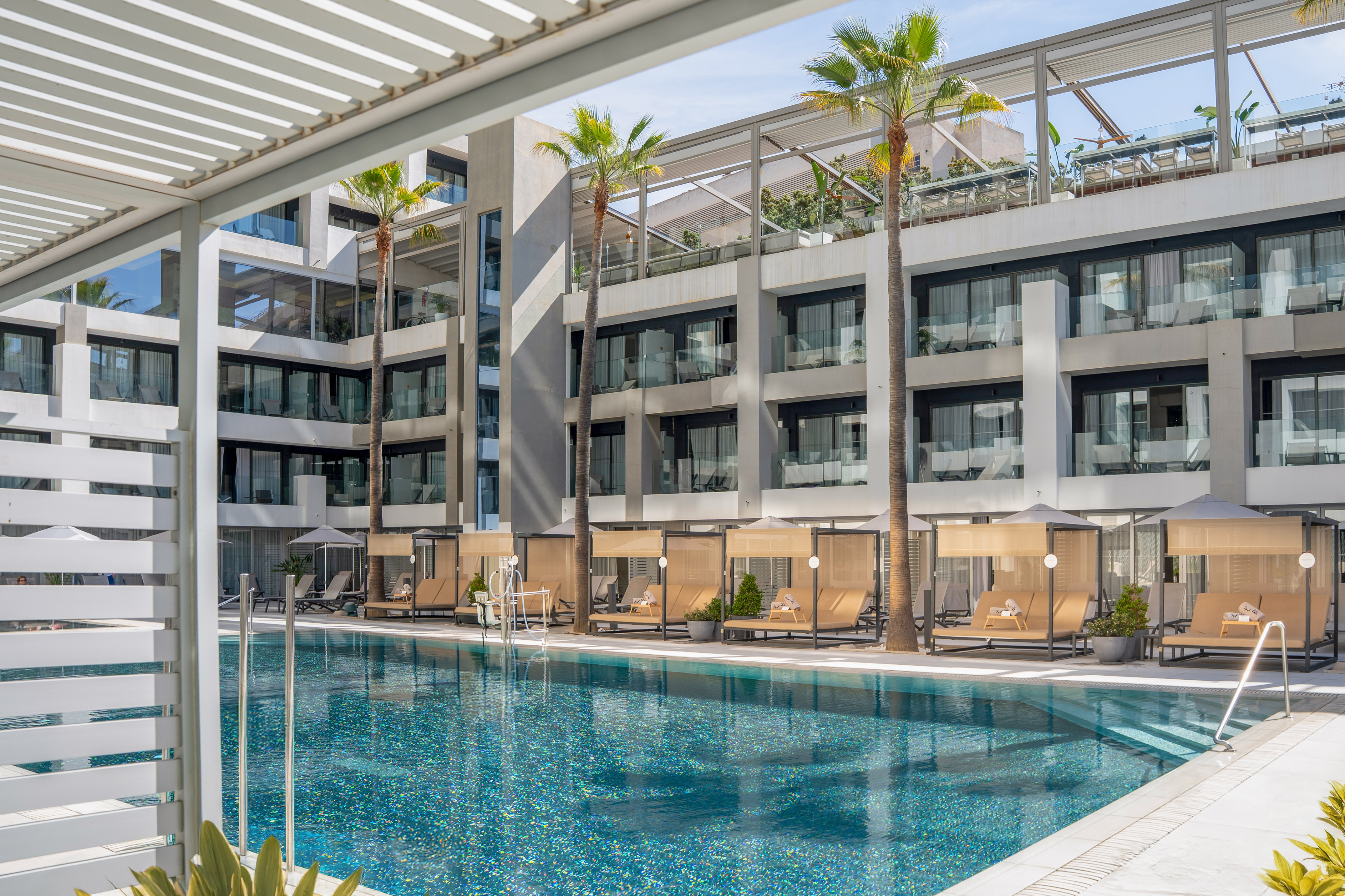 Sparkling blue hotel pool with modern architecture, palm trees, and poolside daybeds.