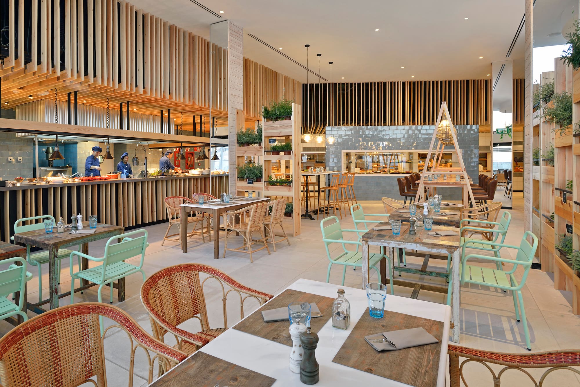 Restaurant interior with open kitchen, buffet, wooden decor, and various seating.