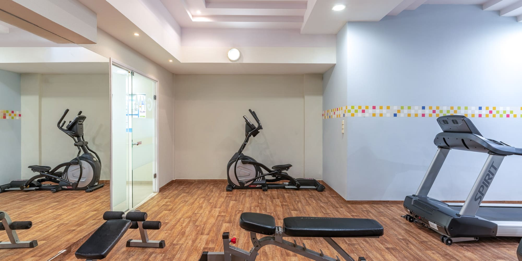 Hotel gym with various exercise equipment: treadmill, elliptical, weight bench.