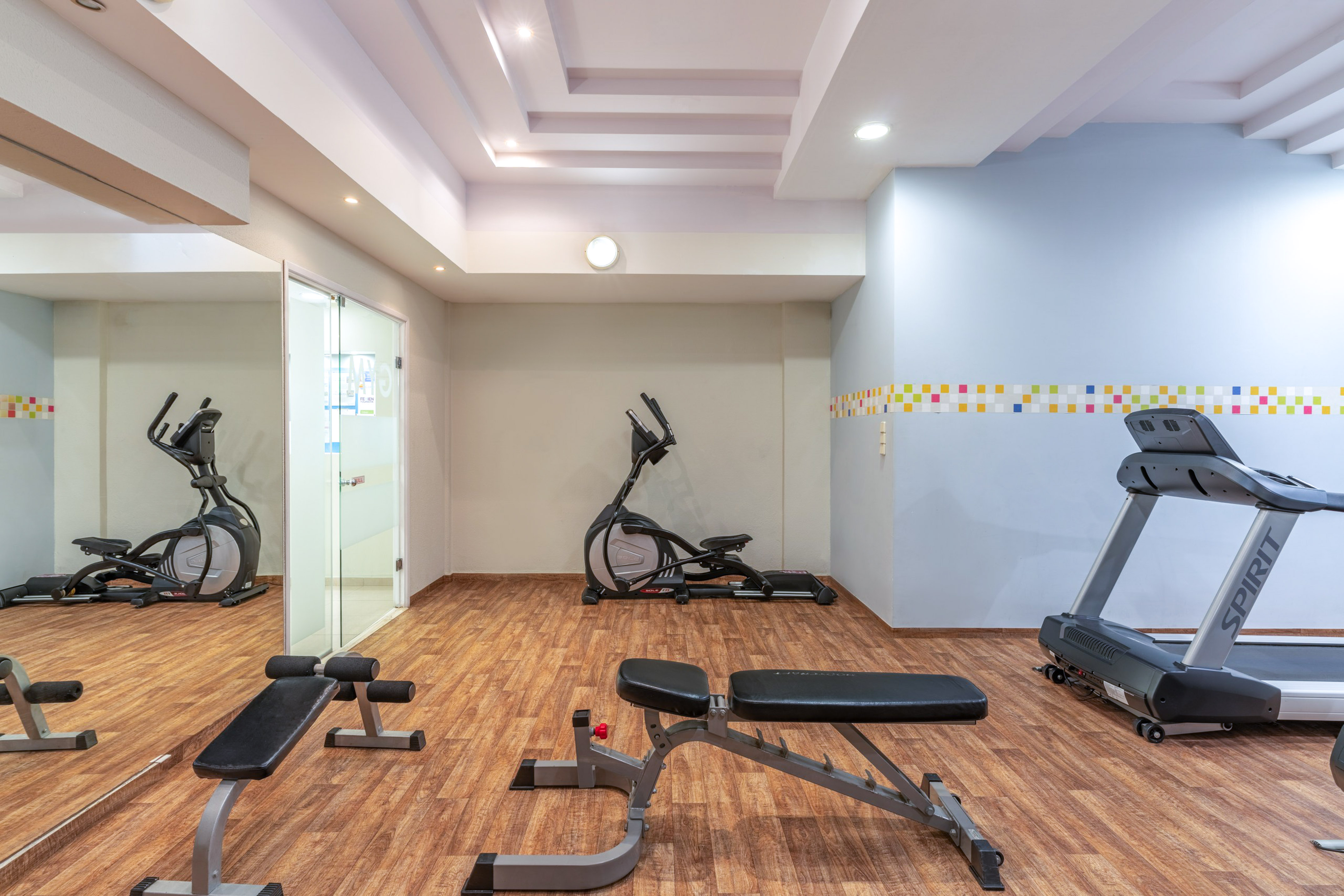 Hotel gym with various exercise equipment: treadmill, elliptical, weight bench.