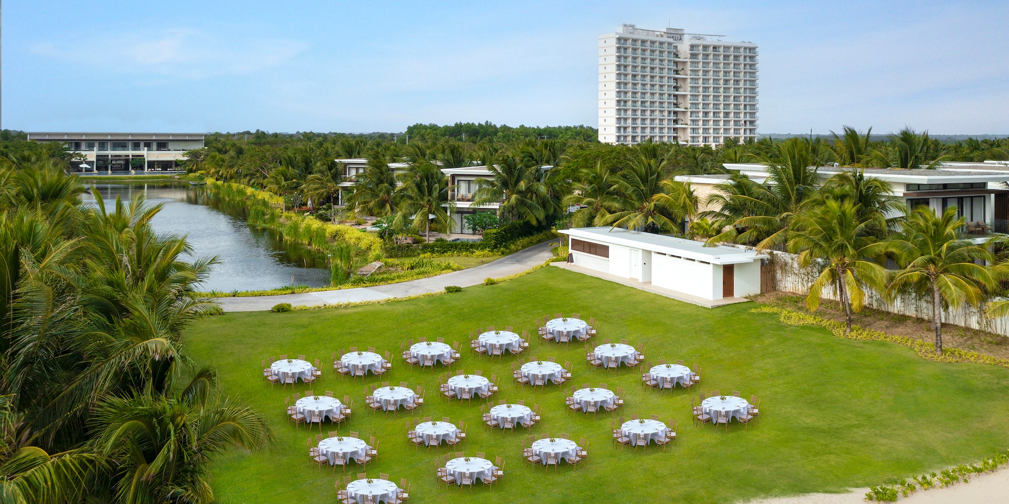 a group of tables on a lawn with a body of water and buildings in the background