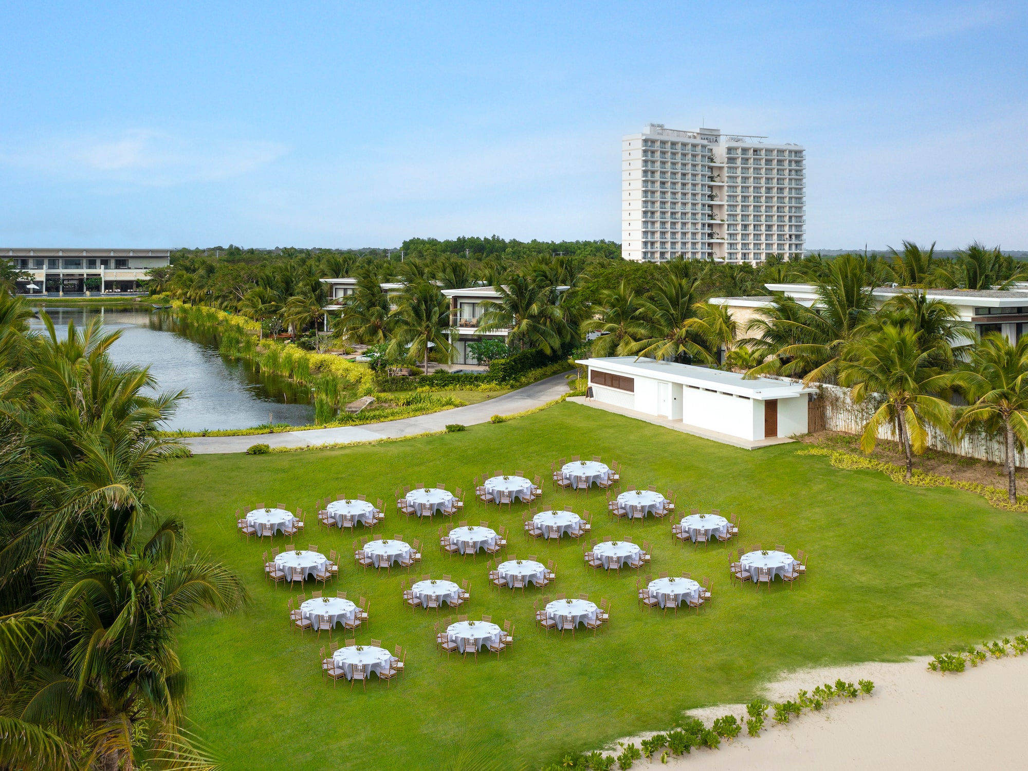 a group of tables on a lawn with a body of water and buildings in the background
