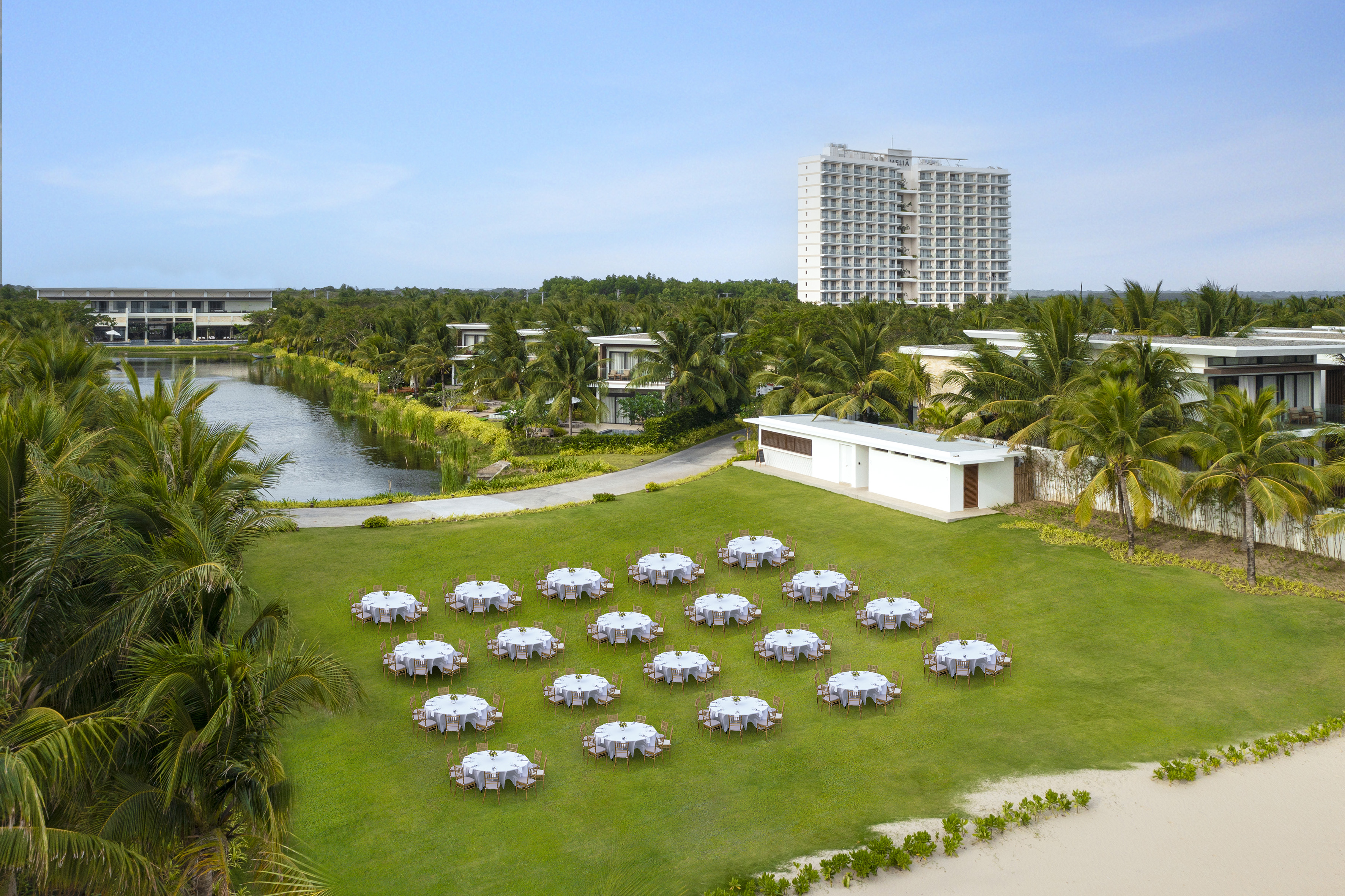 a group of tables on a lawn with a body of water and buildings in the background