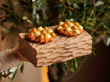 a person holding a piece of wood with food on it