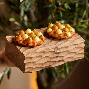 a person holding a piece of wood with food on it