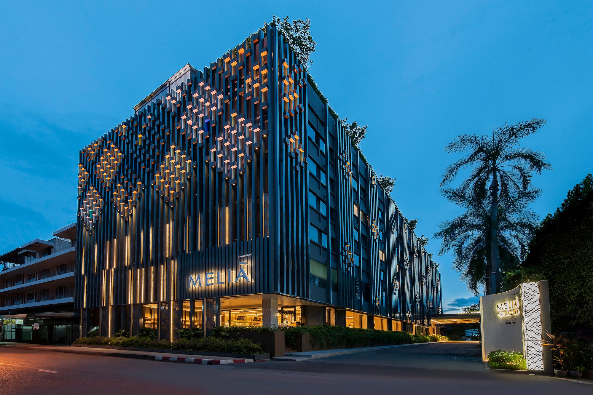 Melia Chiang Mai hotel with illuminated modern facade at dusk, palm tree.