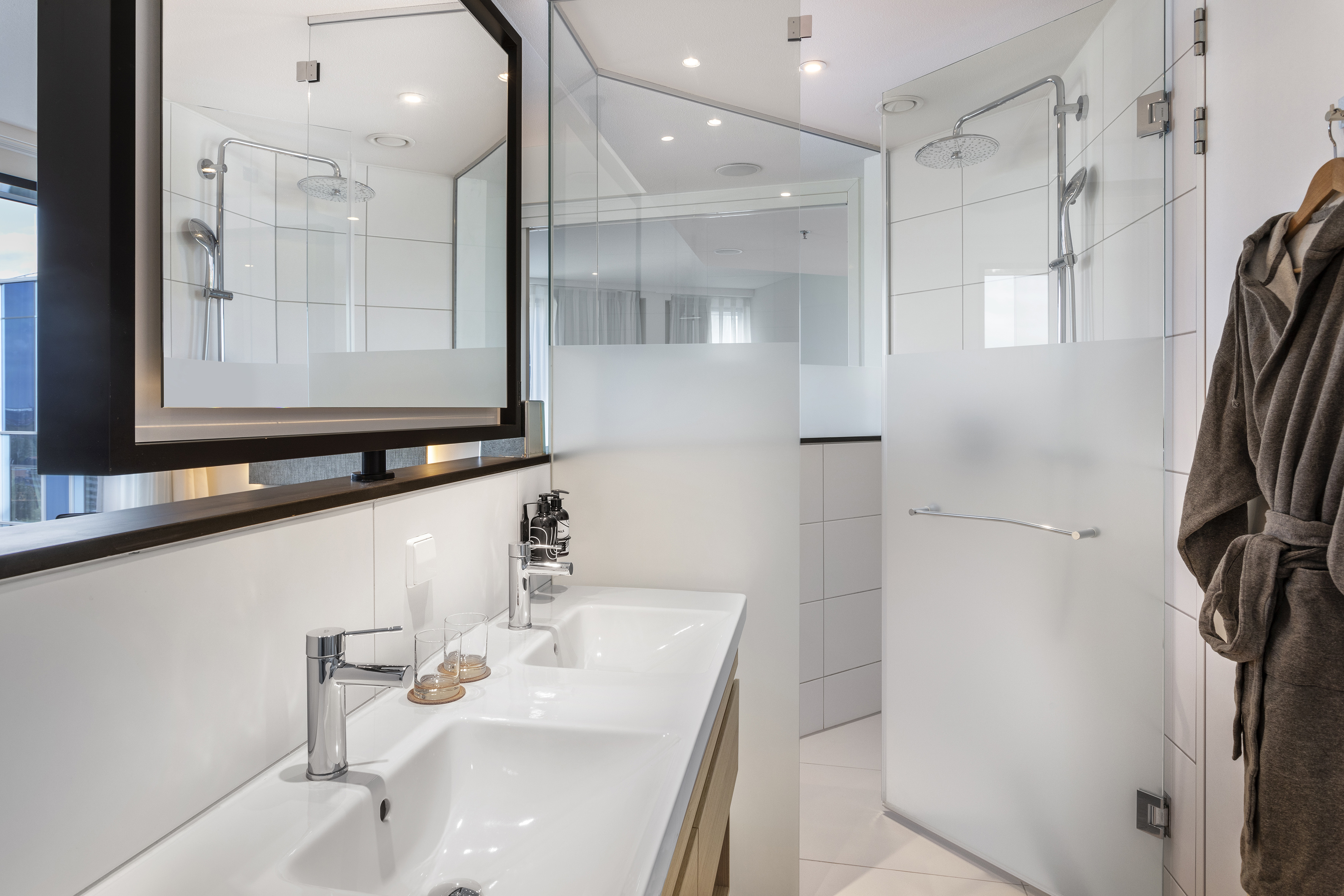 Modern hotel bathroom: double vanity, rain shower, and glass enclosure.