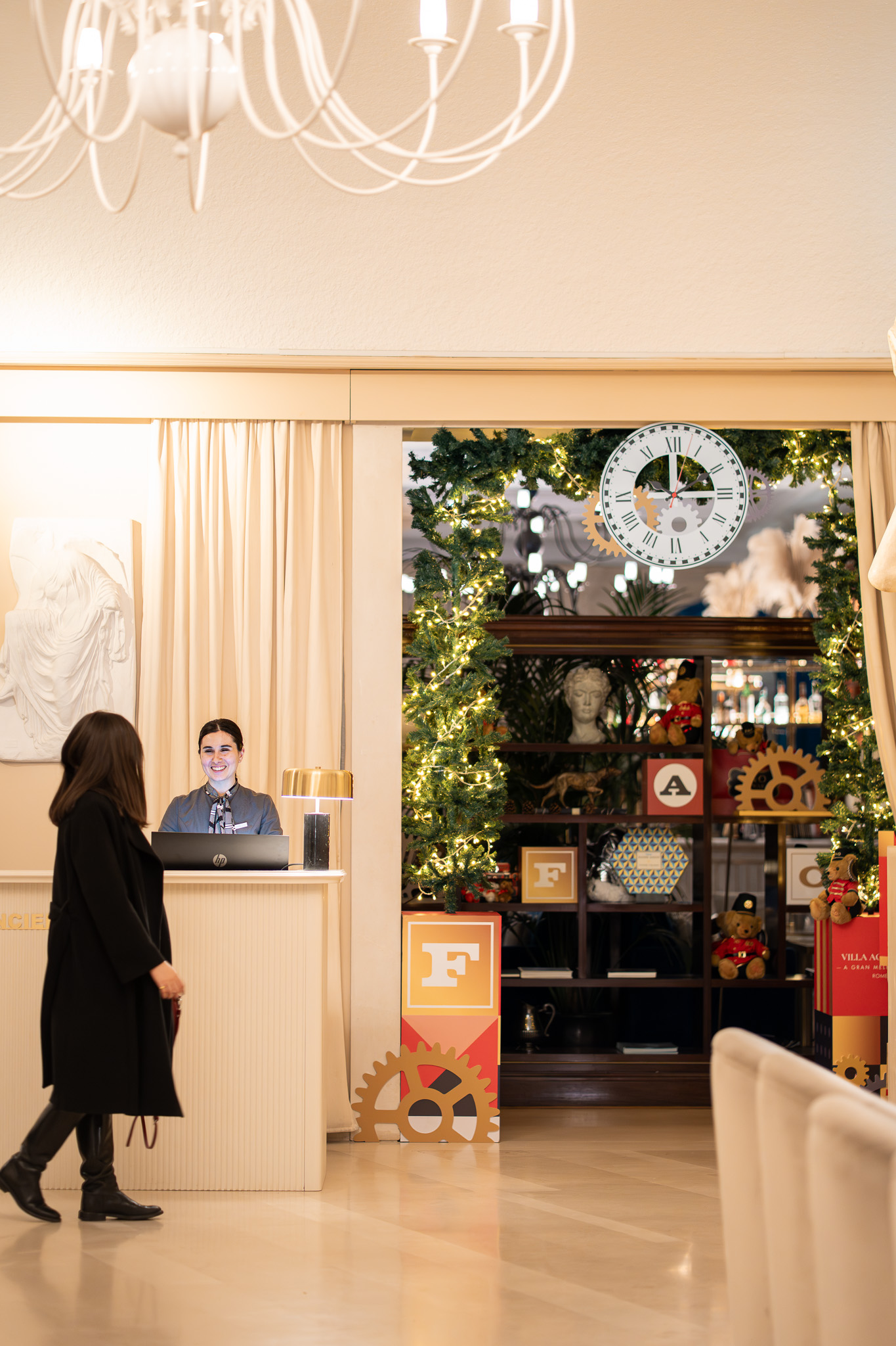 Smiling hotel receptionist and guest in a festive lobby with clock and gears decor.