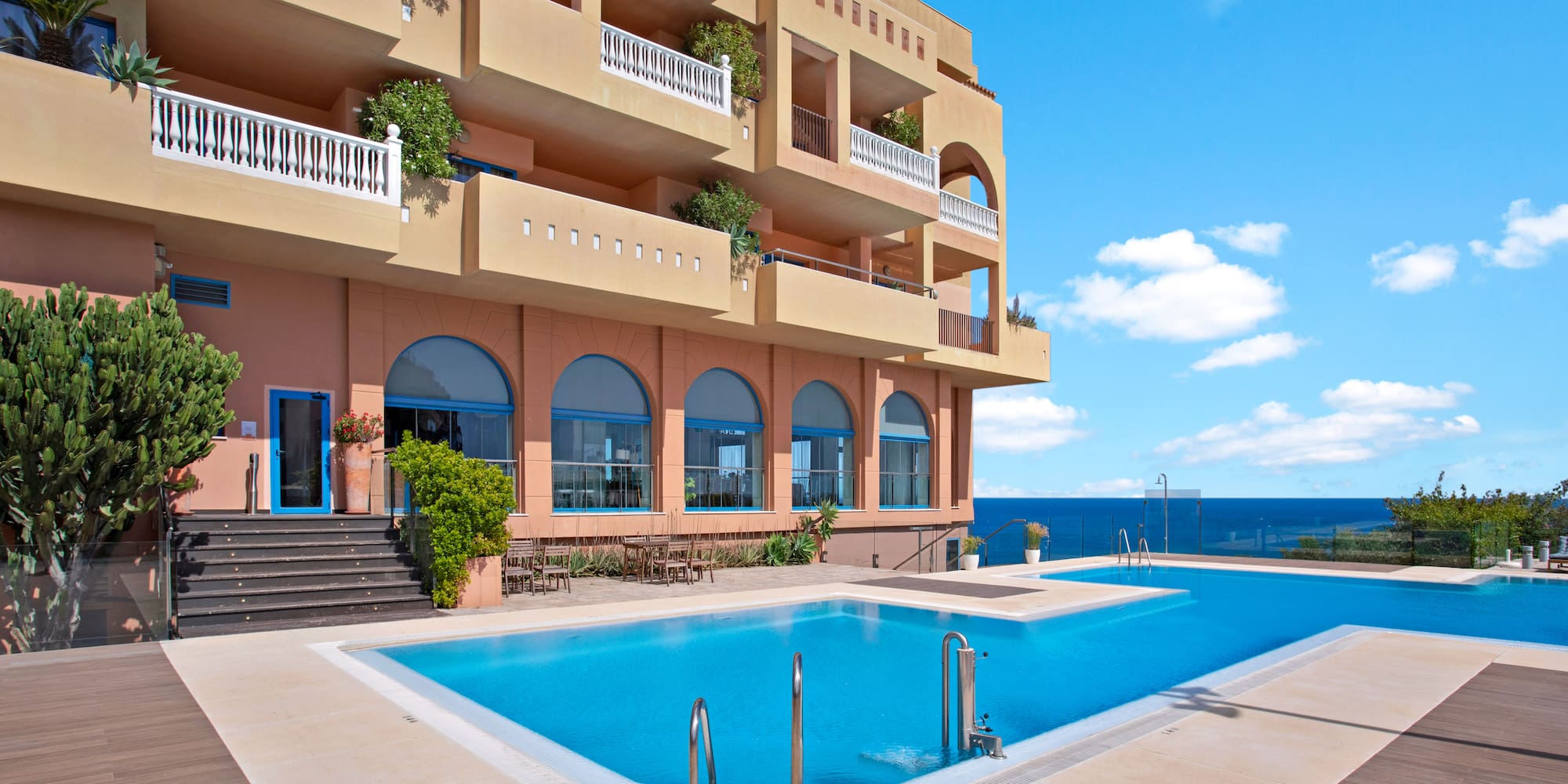 Luxury hotel with ocean view infinity pool, balconies, and blue sky.