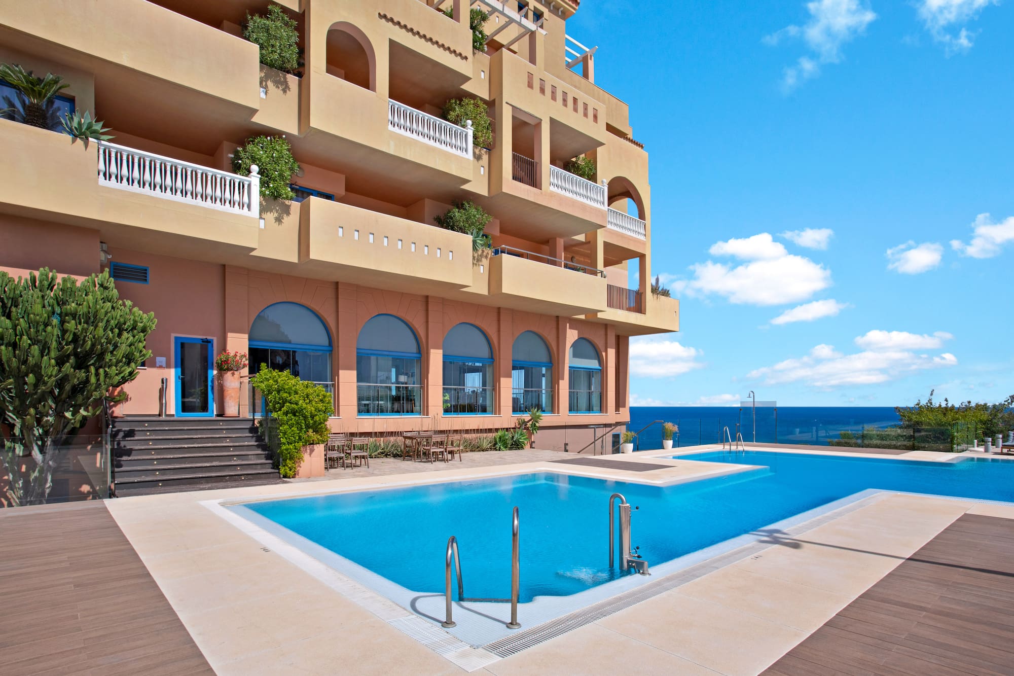 Luxury hotel with ocean view infinity pool, balconies, and blue sky.