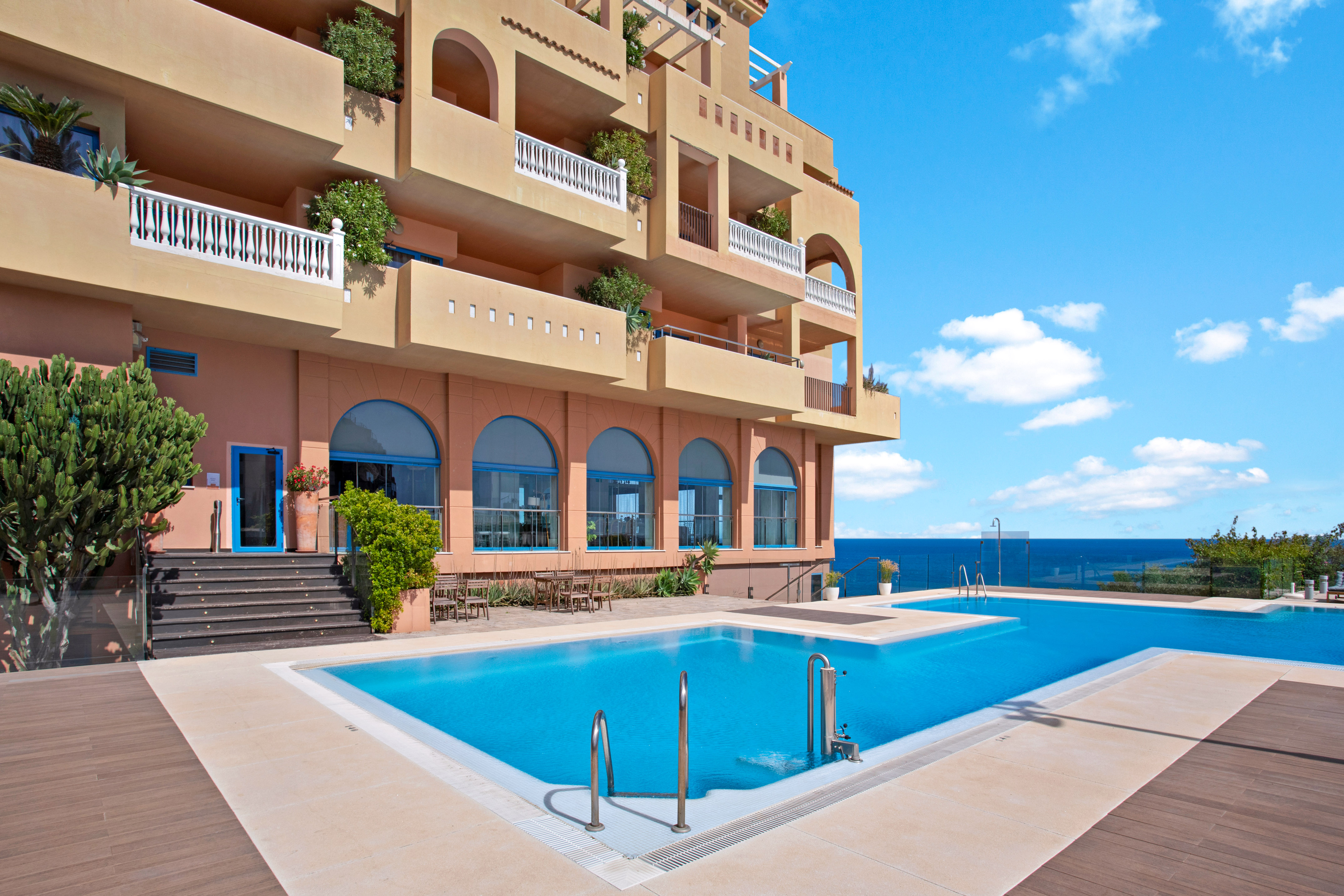 Luxury hotel with ocean view infinity pool, balconies, and blue sky.