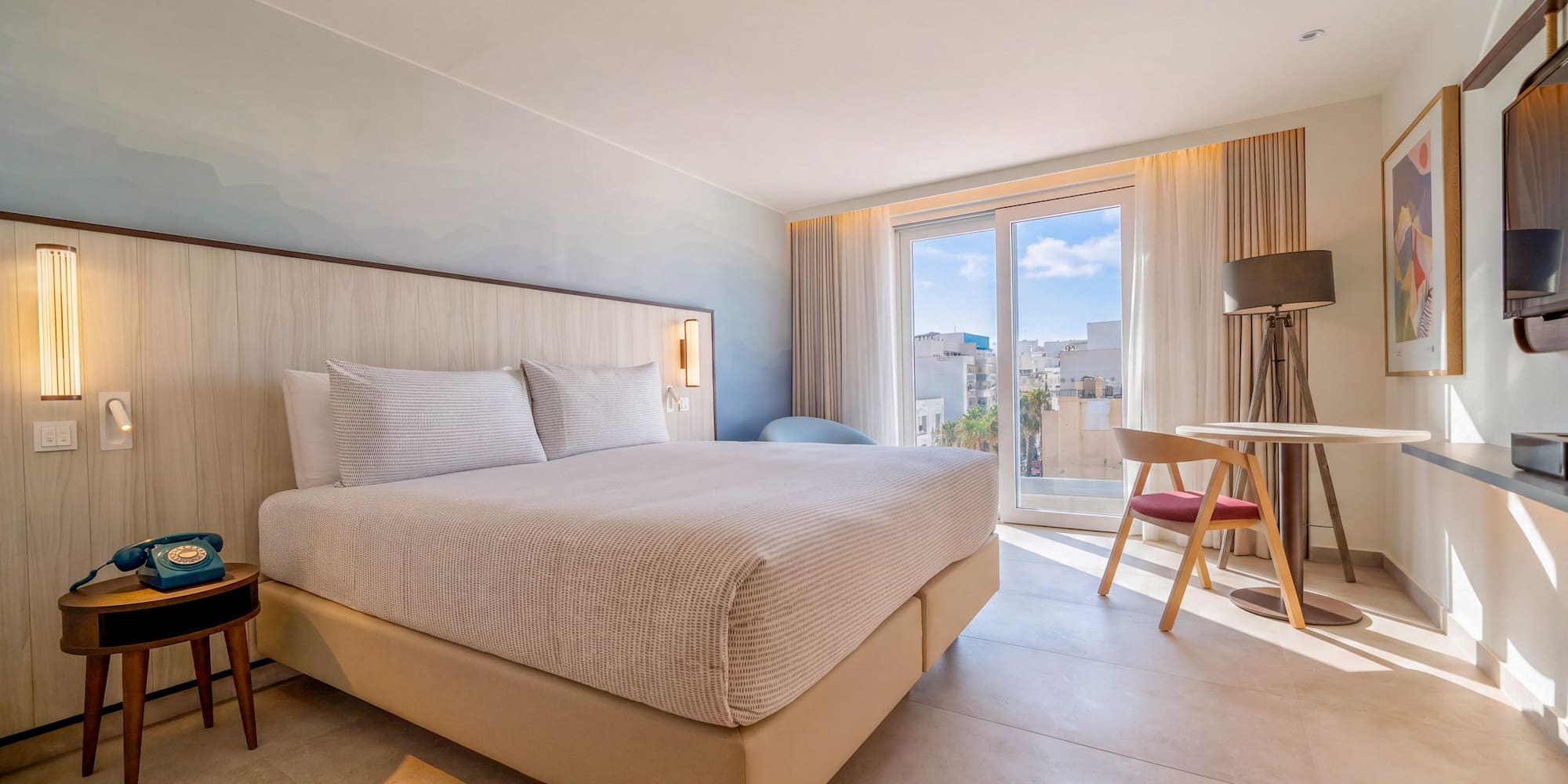 Modern hotel bedroom with king bed, city view balcony, and chic design.