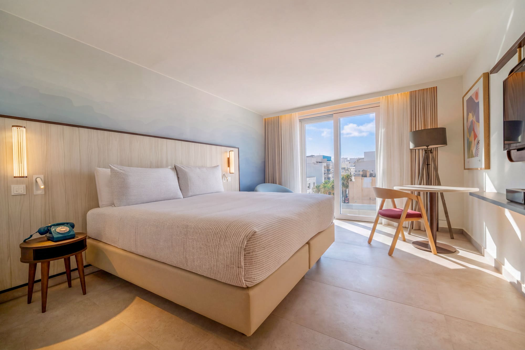 Modern hotel bedroom with king bed, city view balcony, and chic design.