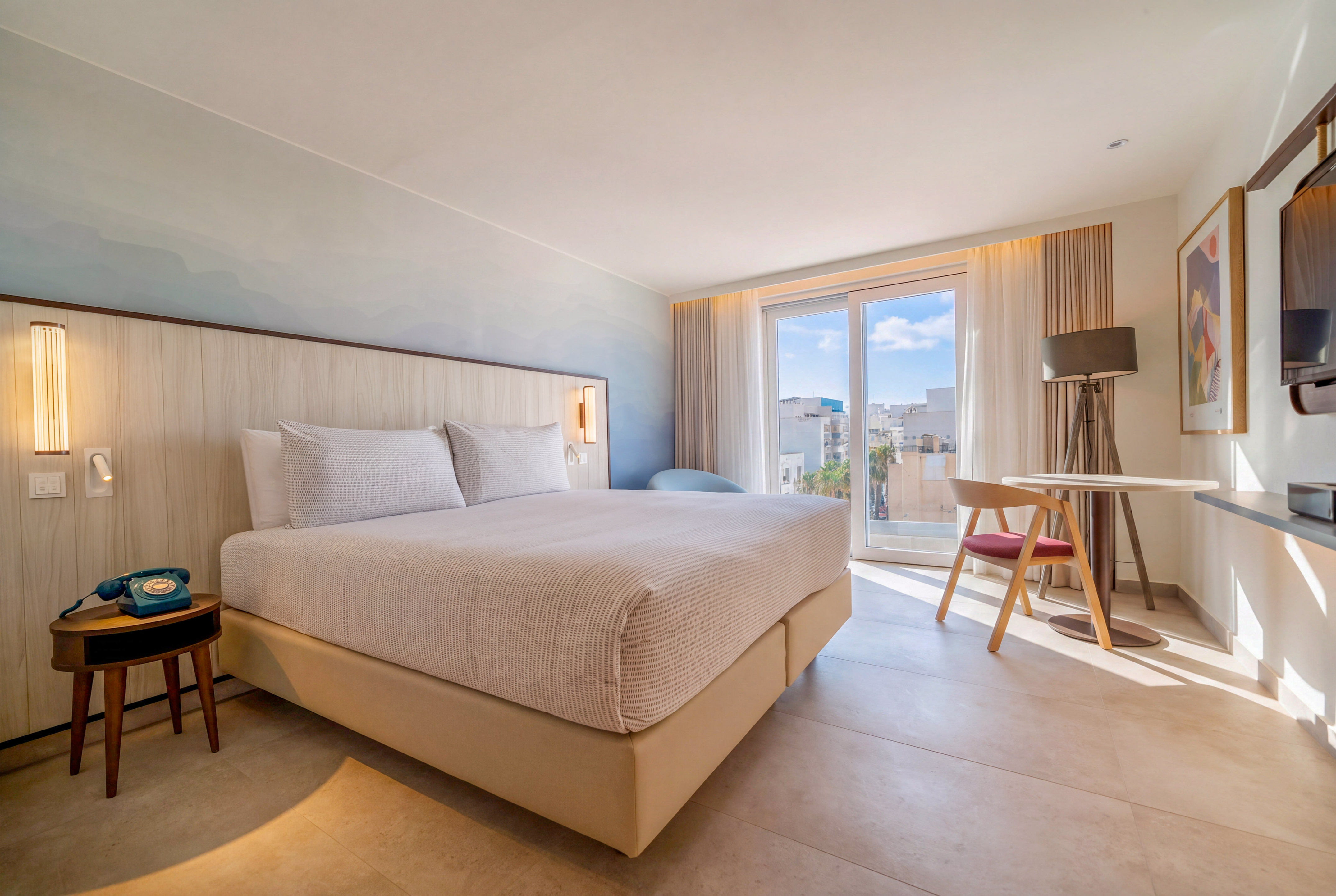 Modern hotel bedroom with king bed, city view balcony, and chic design.