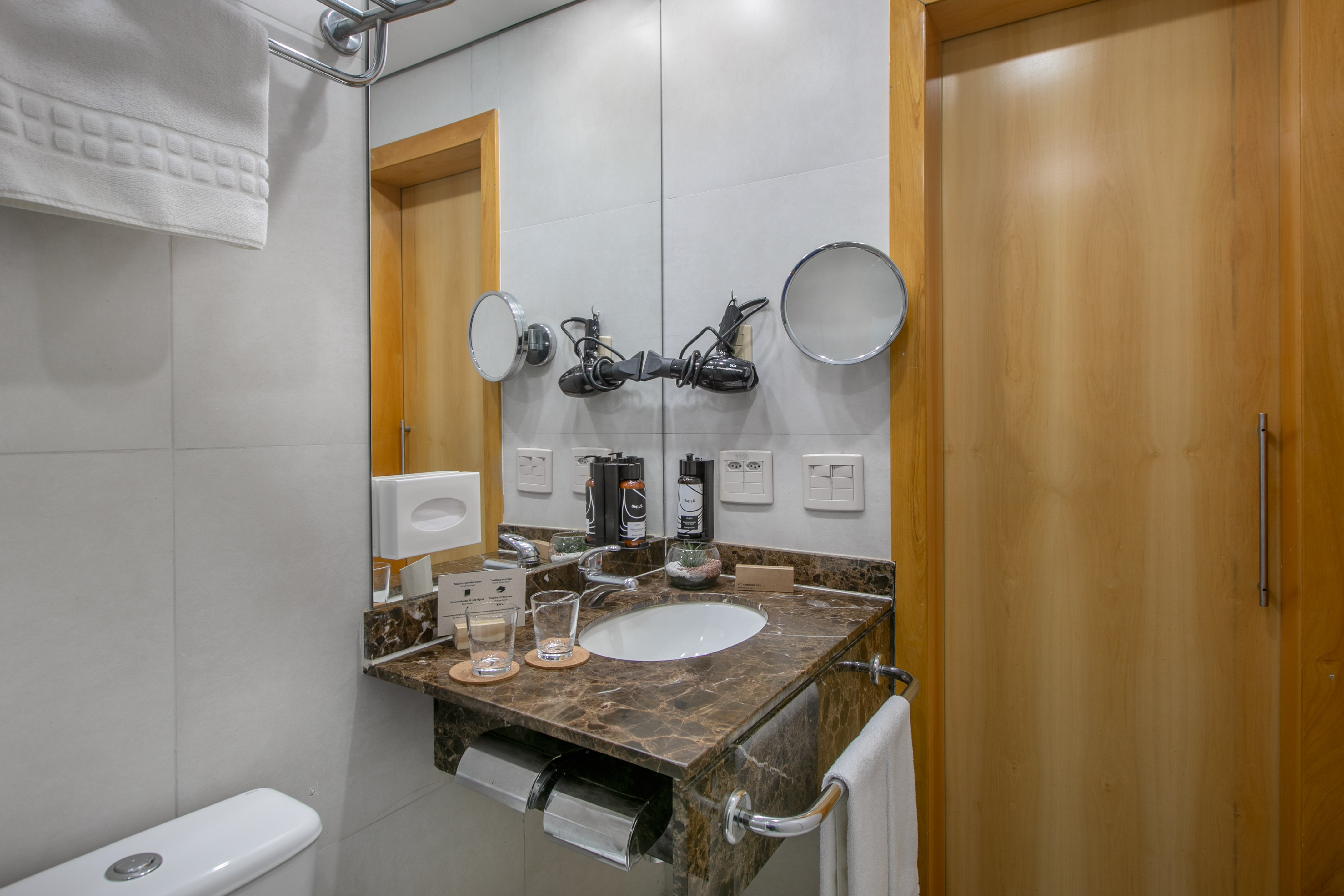 Hotel bathroom with marble vanity, sink, mirror, hairdryer, and toilet.