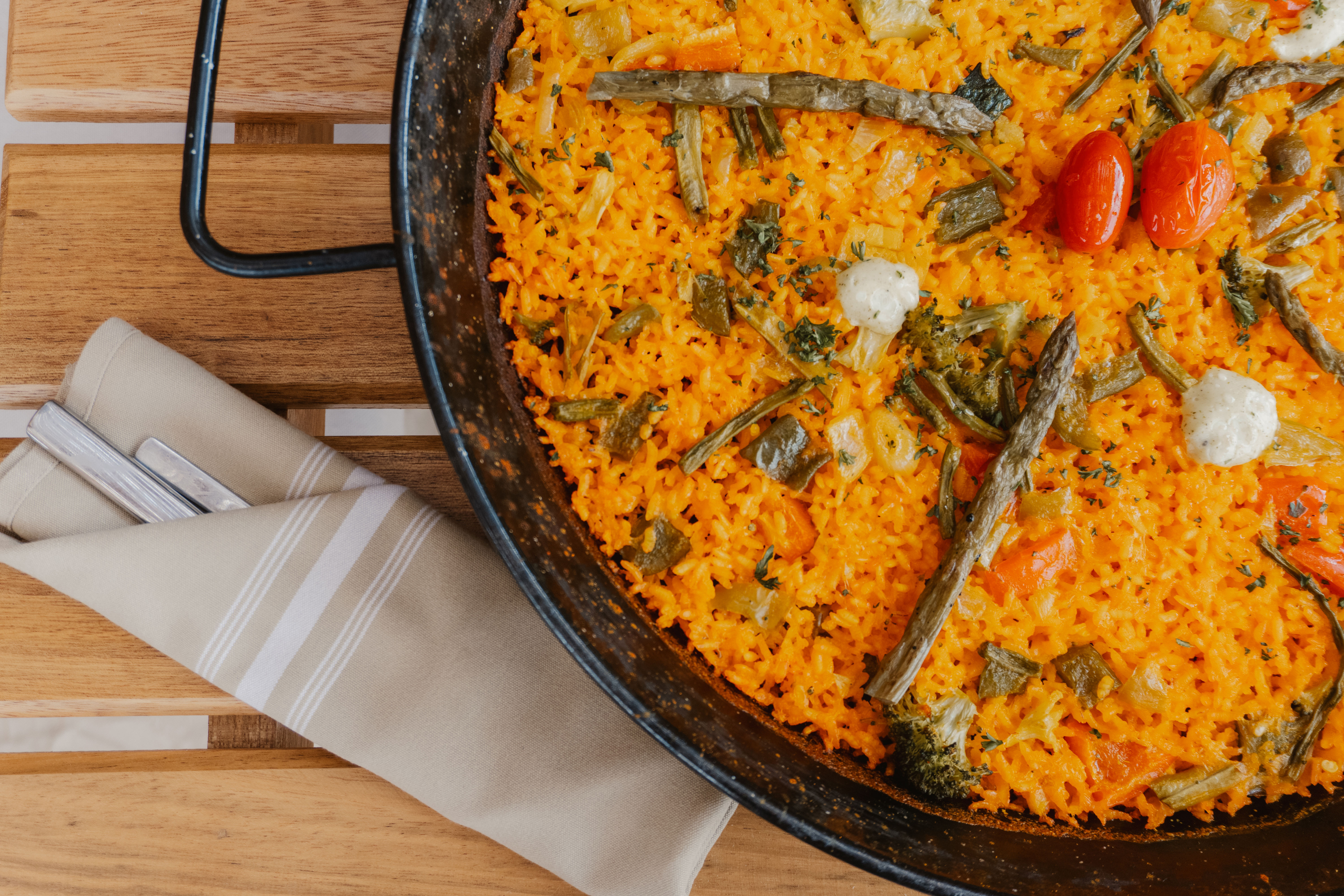 Vegetable paella in black pan with asparagus, tomatoes, orange rice.