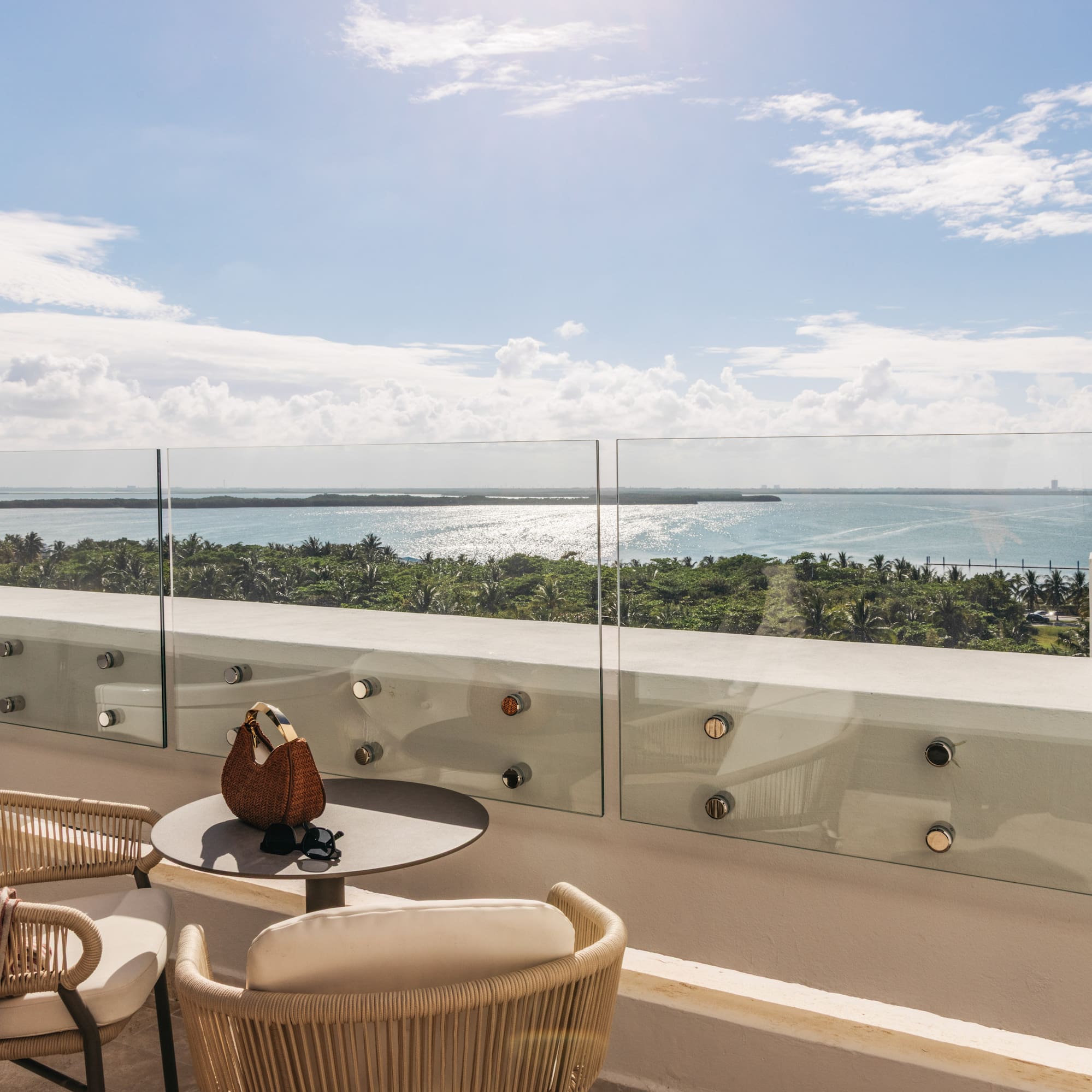 Tropical balcony with outdoor seating, glass railing, and sparkling ocean view.