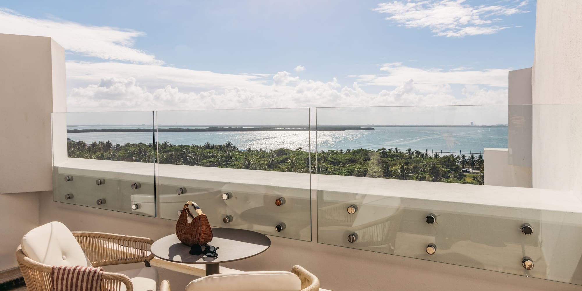 Tropical balcony with outdoor seating, glass railing, and sparkling ocean view.