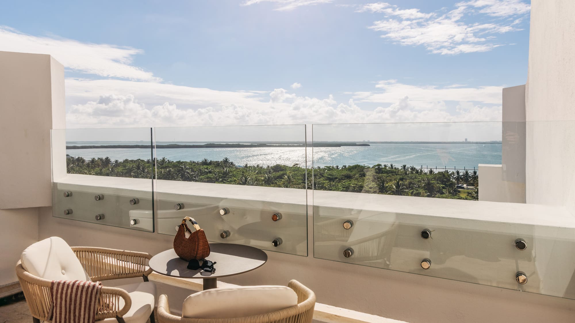 Tropical balcony with outdoor seating, glass railing, and sparkling ocean view.
