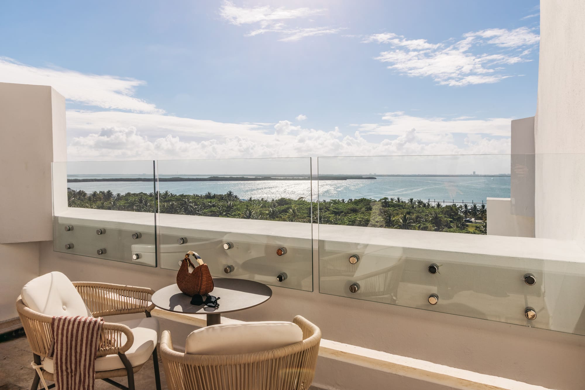 Tropical balcony with outdoor seating, glass railing, and sparkling ocean view.