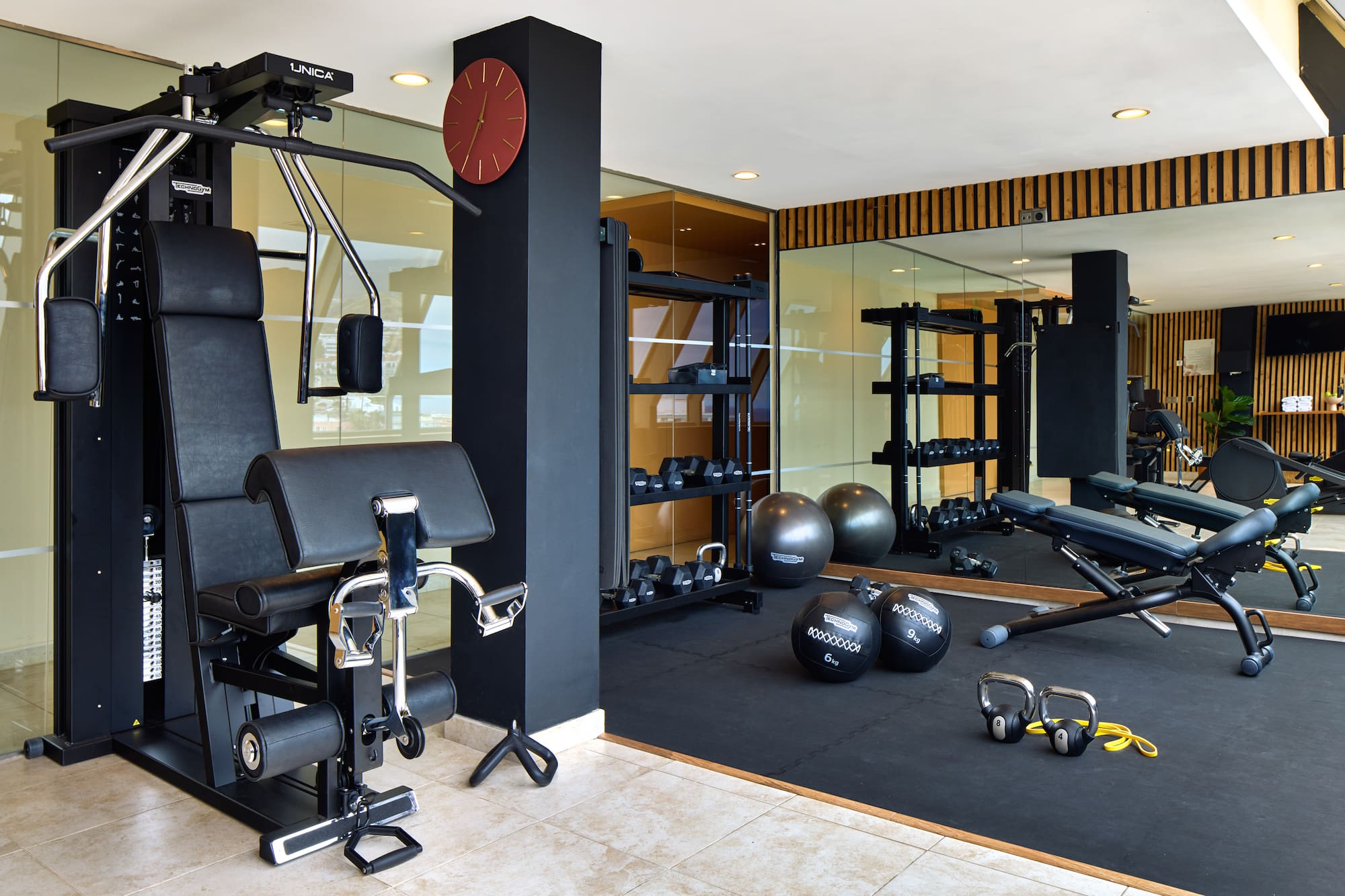 Modern gym with multi-station machine, dumbbell rack, stability balls, and adjustable bench.