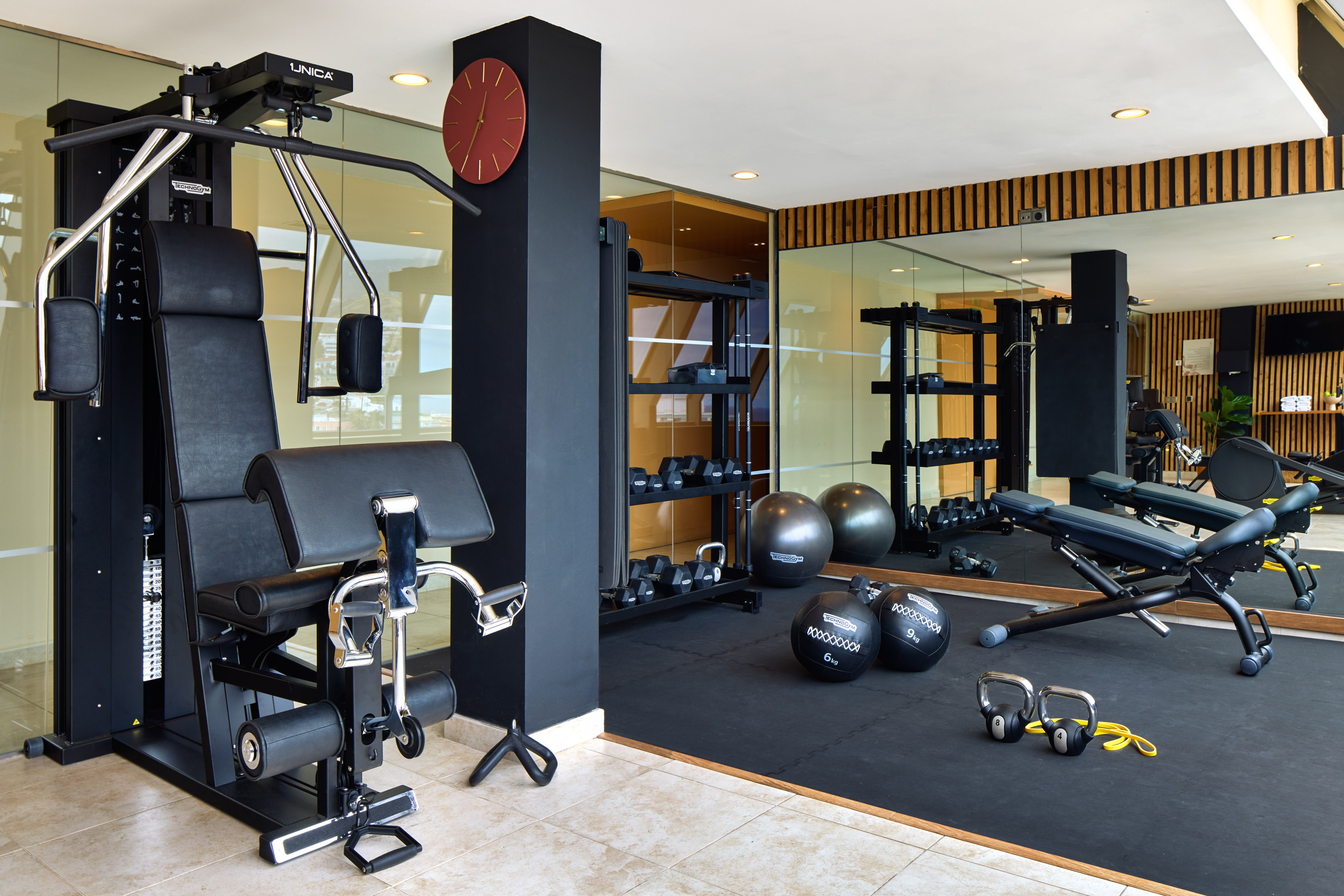 Modern gym with multi-station machine, dumbbell rack, stability balls, and adjustable bench.