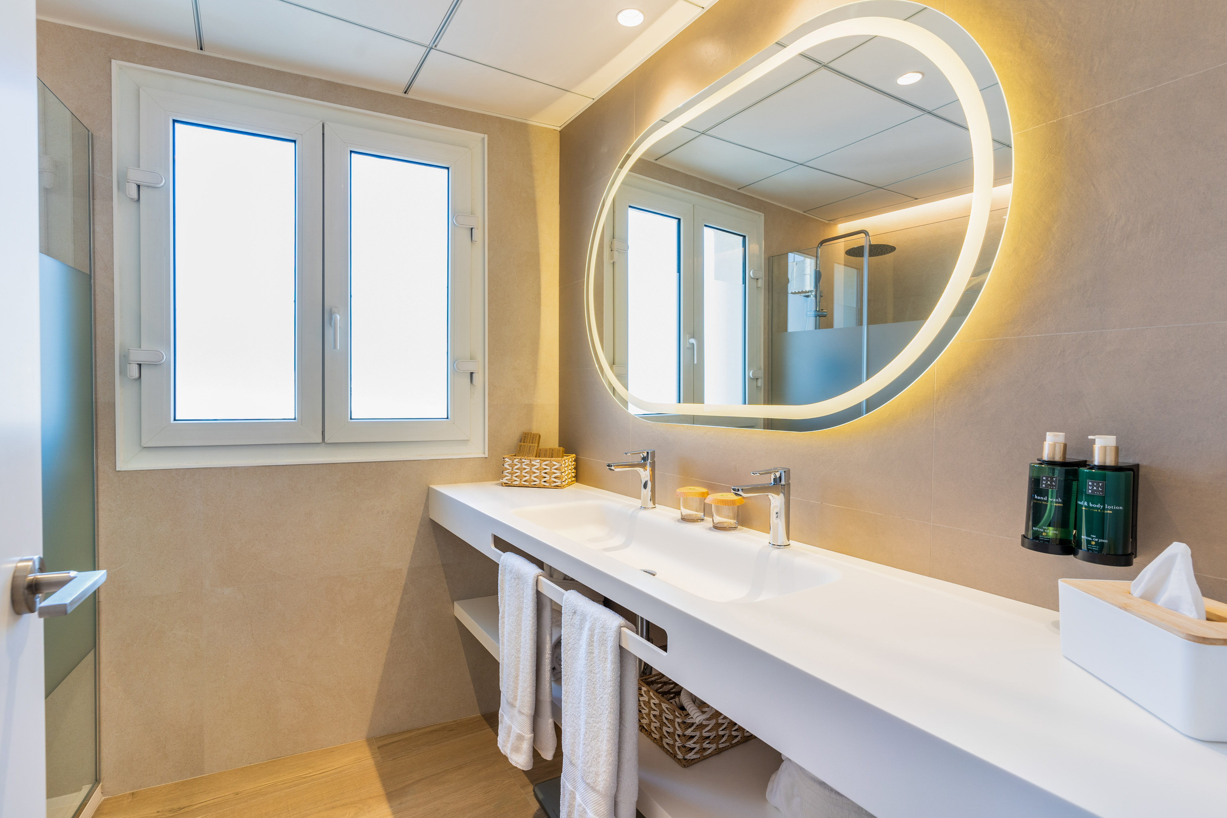 Bright, modern bathroom with double sink vanity and backlit oval mirror.