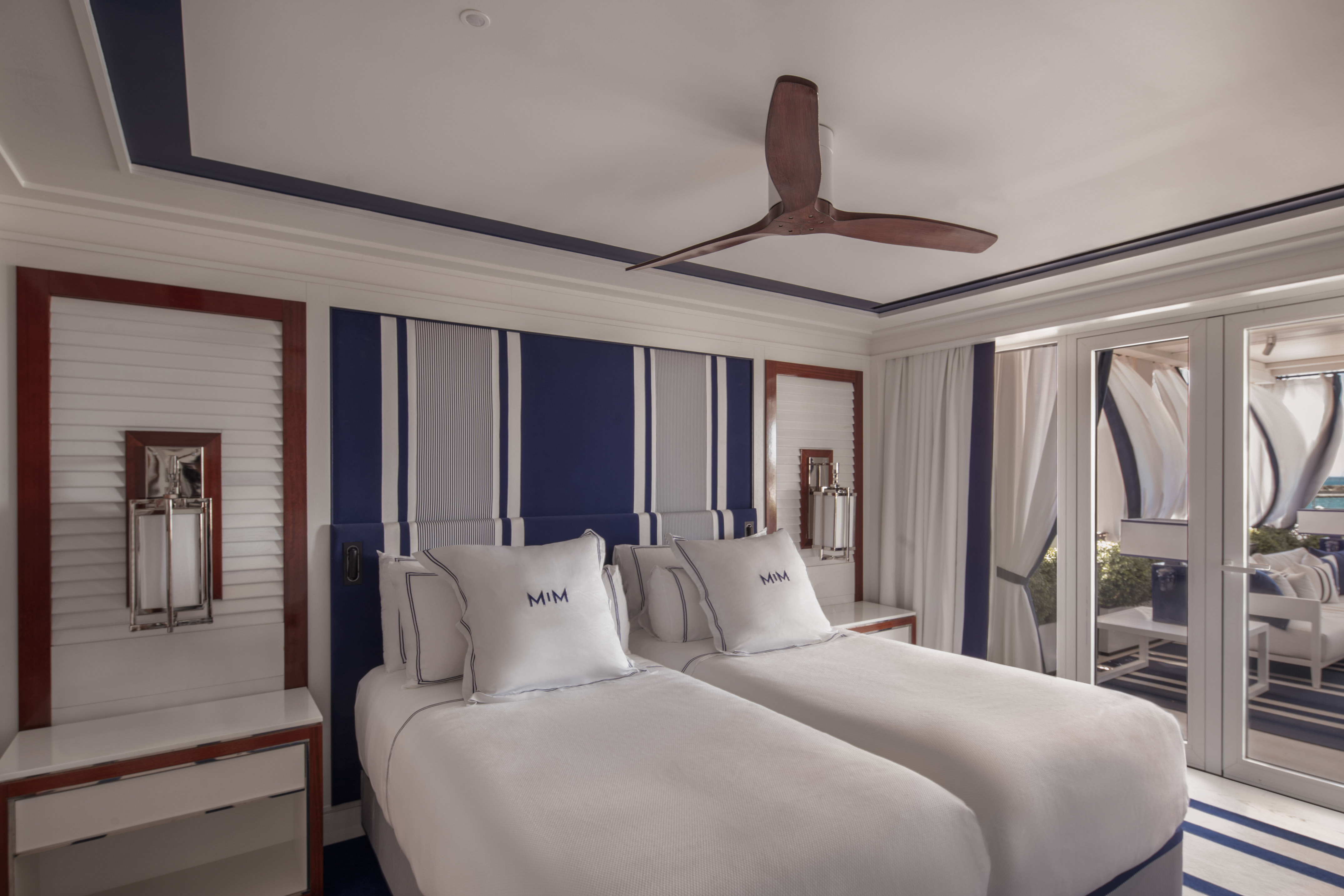 Coastal twin bedroom with blue & white stripes, ceiling fan, and French doors.