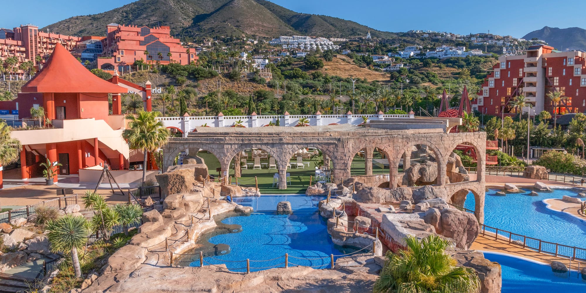 Resort water park with blue pools, rock features, arches, and mountain landscape.