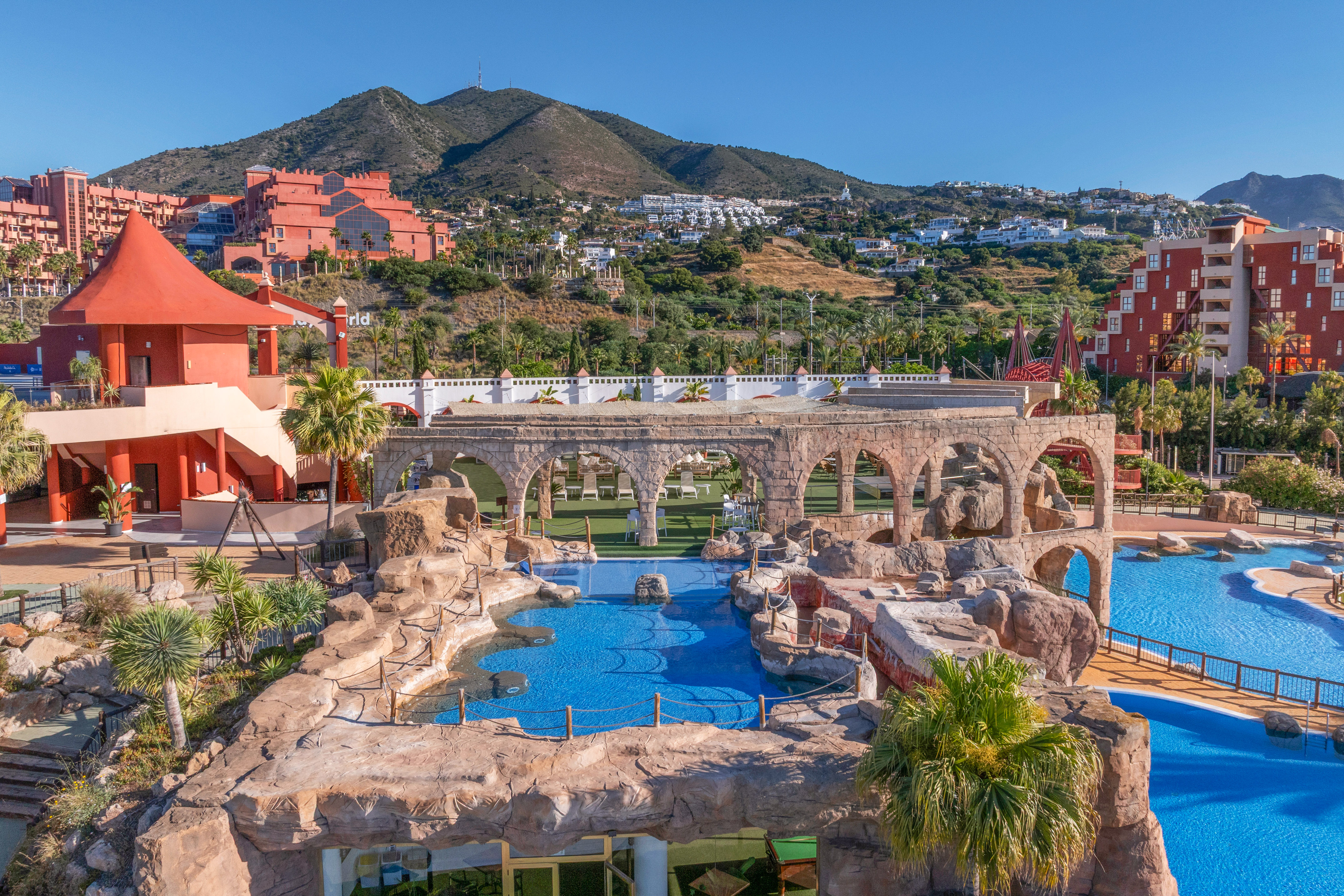 Resort water park with blue pools, rock features, arches, and mountain landscape.