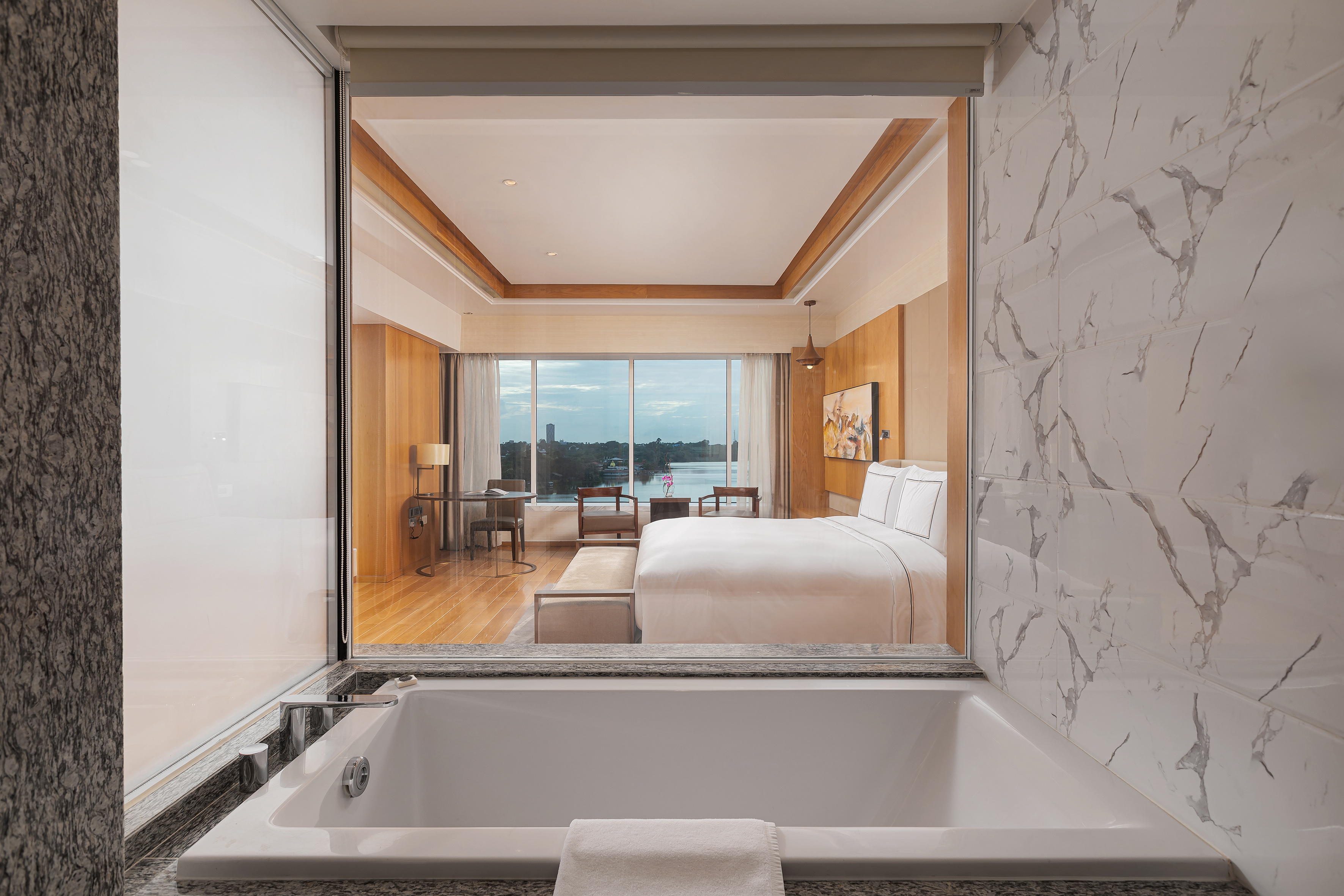 Luxury bathtub looking into modern hotel bedroom with panoramic river view.