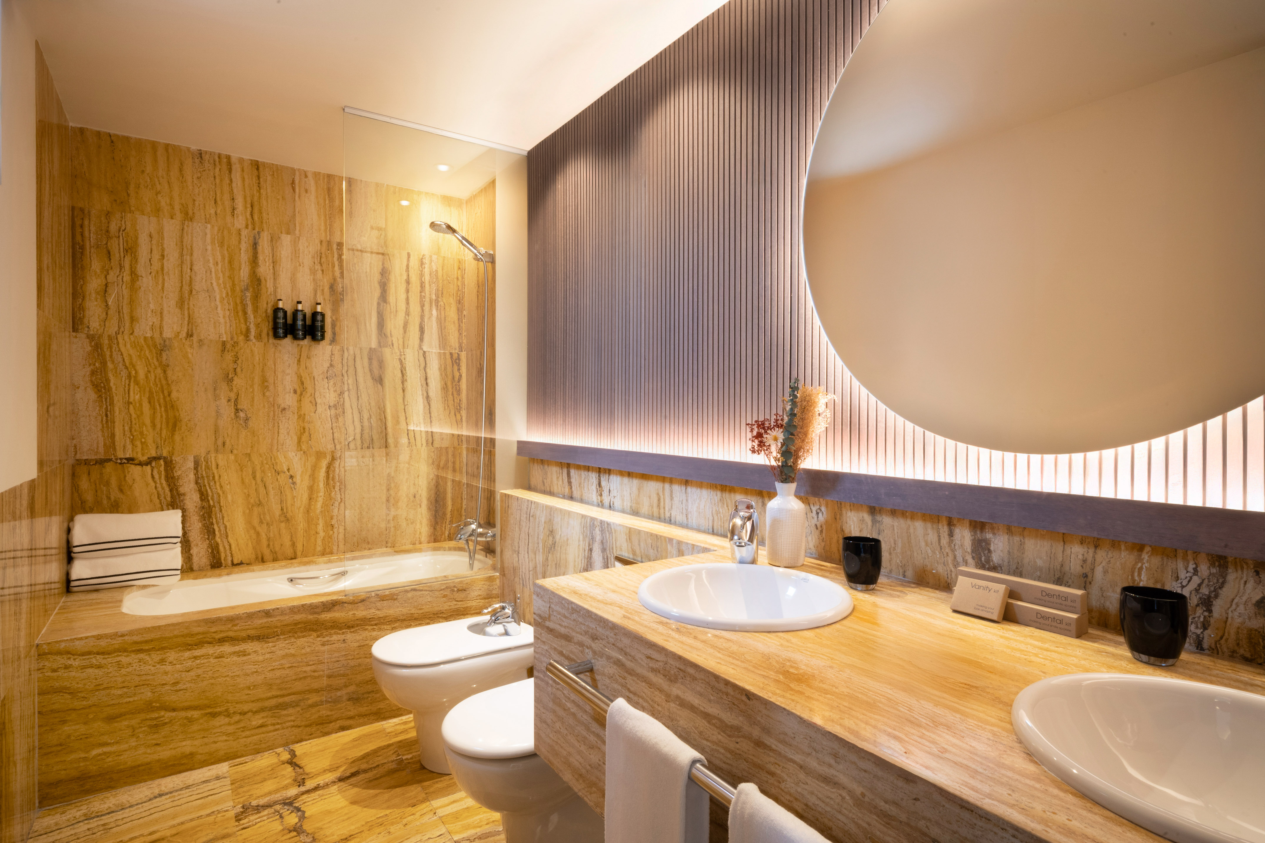 Luxurious travertine bathroom with double vanity, shower, tub, and toilet.