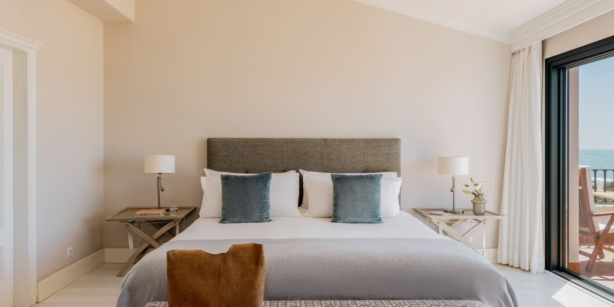 Elegant bedroom with king bed, ocean view balcony, and light decor.