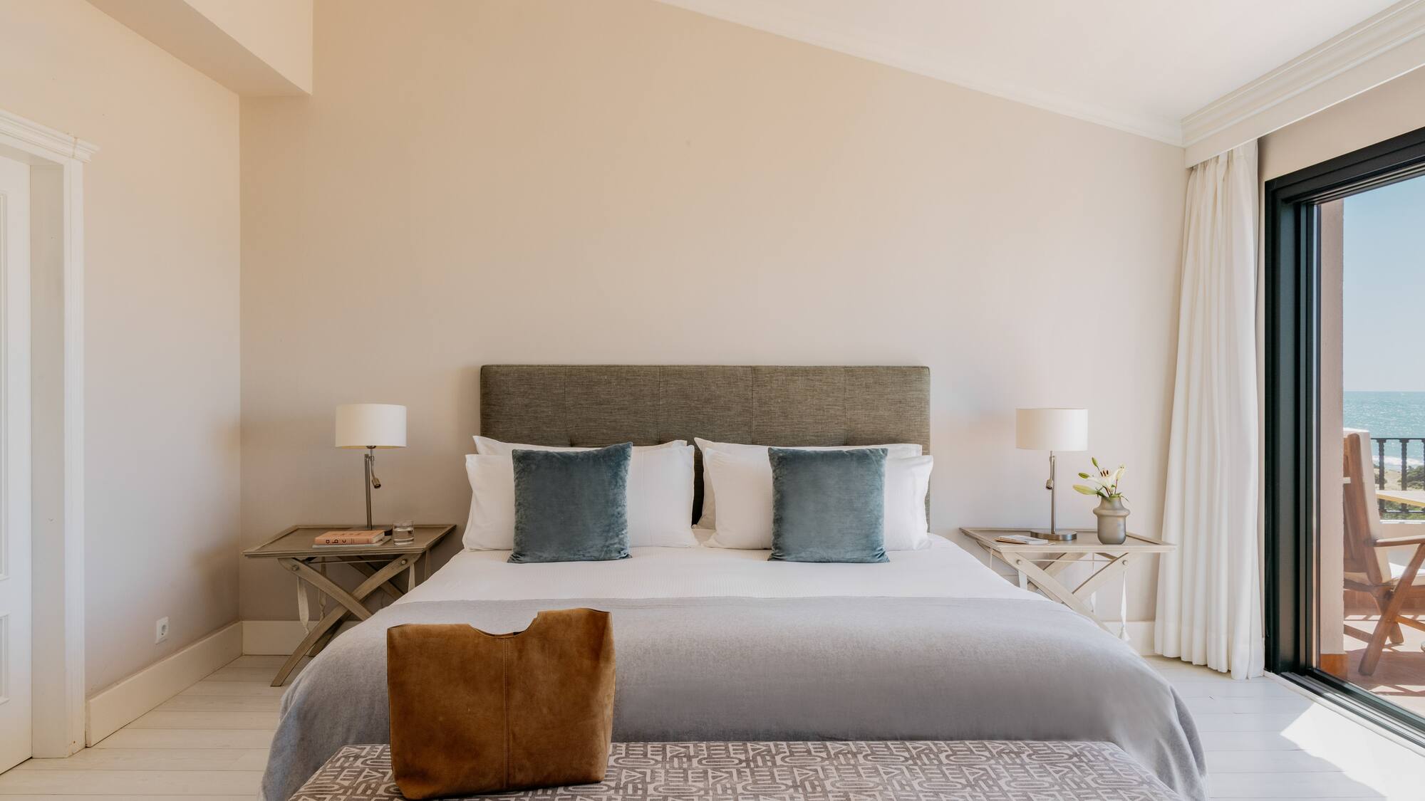 Elegant bedroom with king bed, ocean view balcony, and light decor.