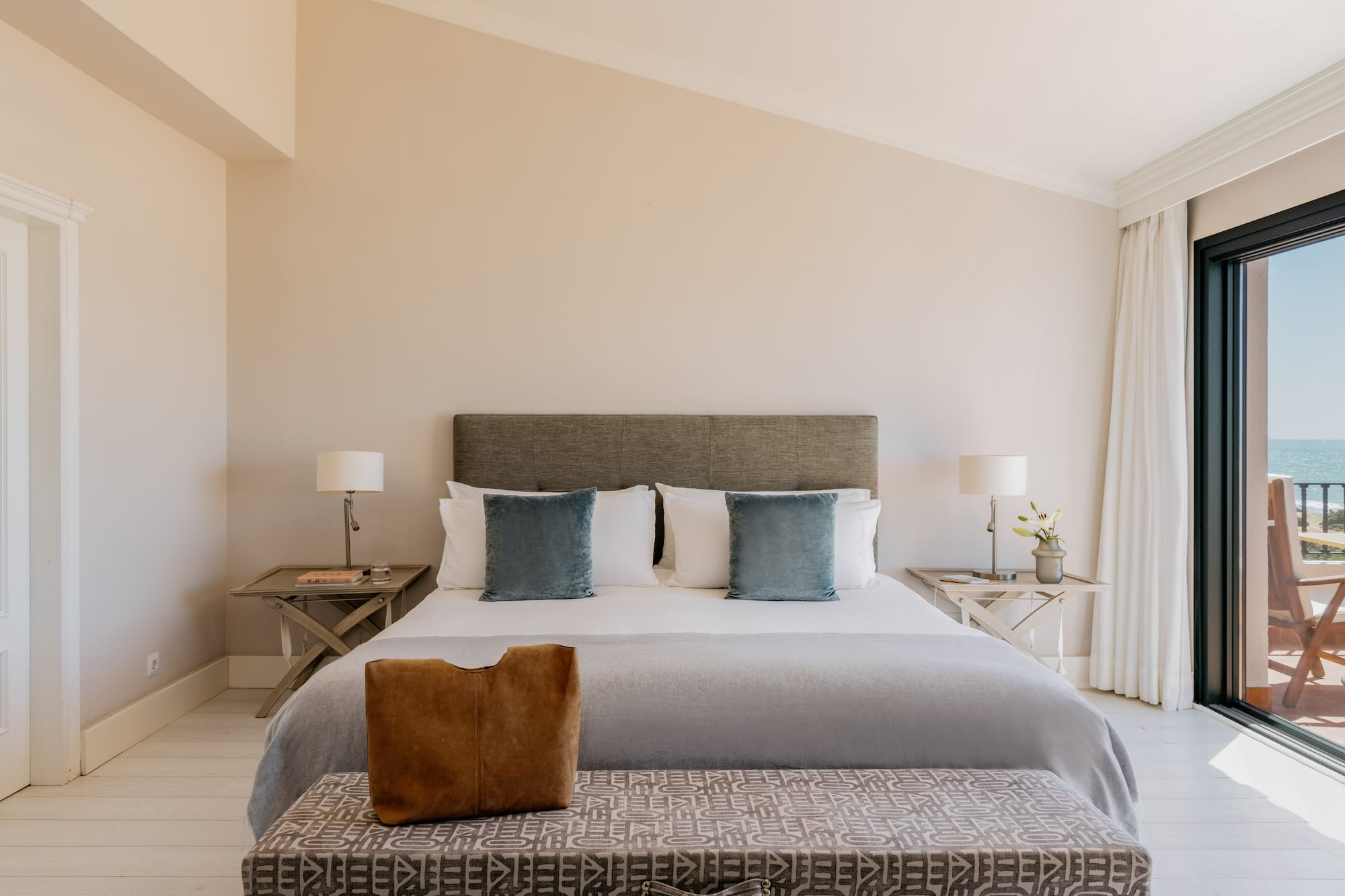 Elegant bedroom with king bed, ocean view balcony, and light decor.